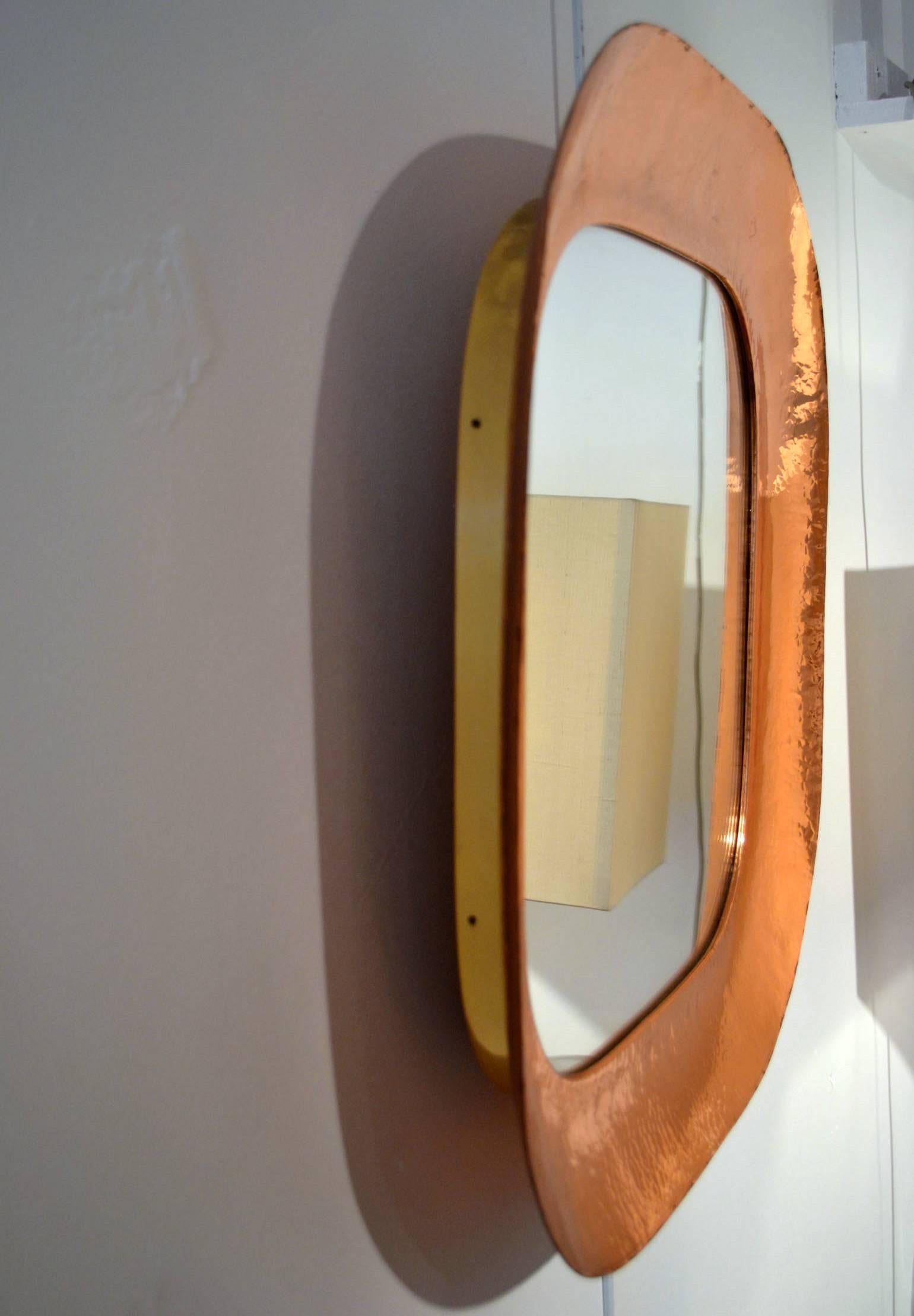 Unusual hand beaten copper mirror with curvaceous corners edges raised from the wall by a brass border.