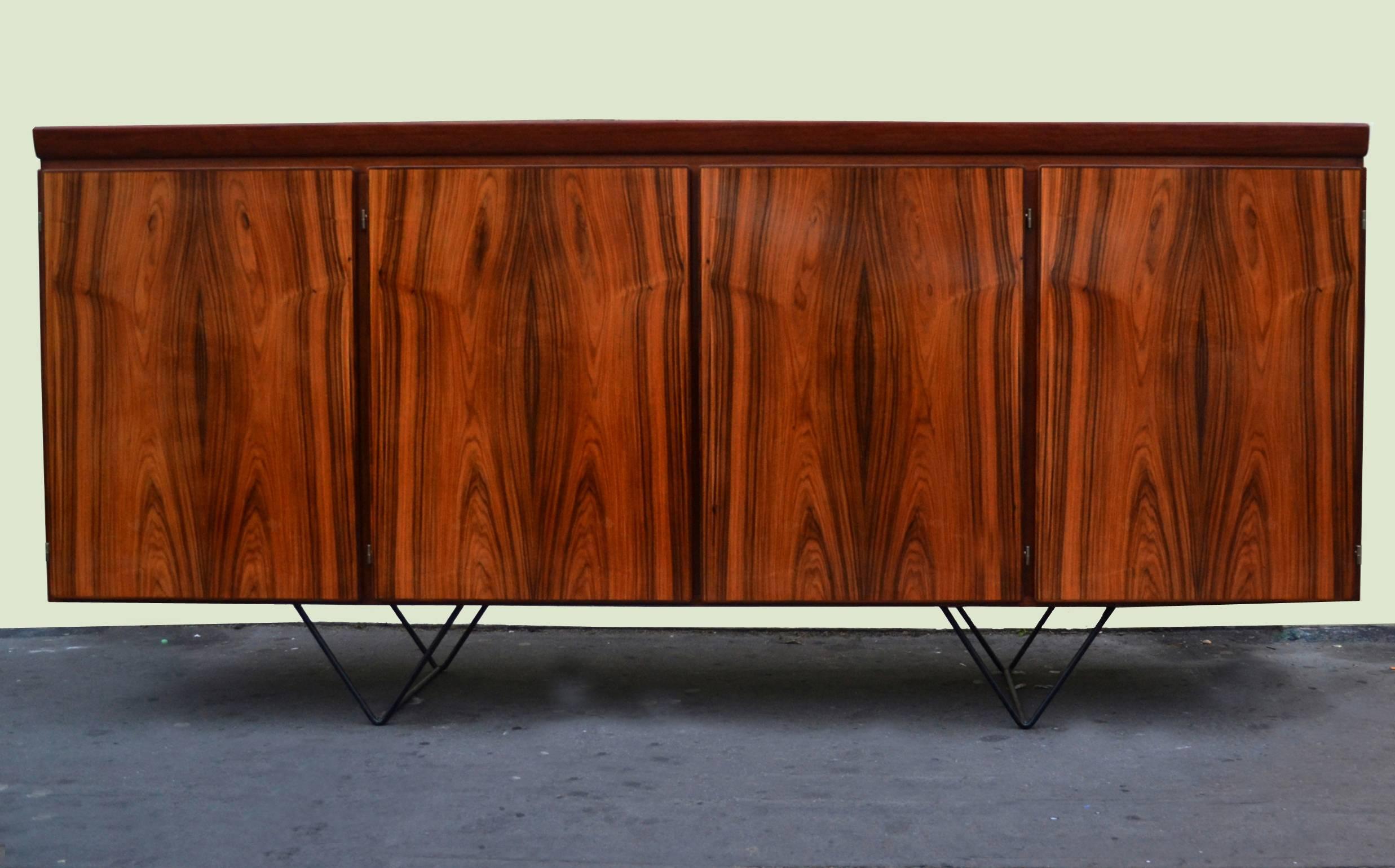 Danish Minimalist credenza in Indian palisander veneer by Skovby Møbelfabrik, made in Denmark stands on metal hairpin legs.
The storage cabinet has four unit with minimal cabinet doors. The three of the units are laid out with shelves and one unit