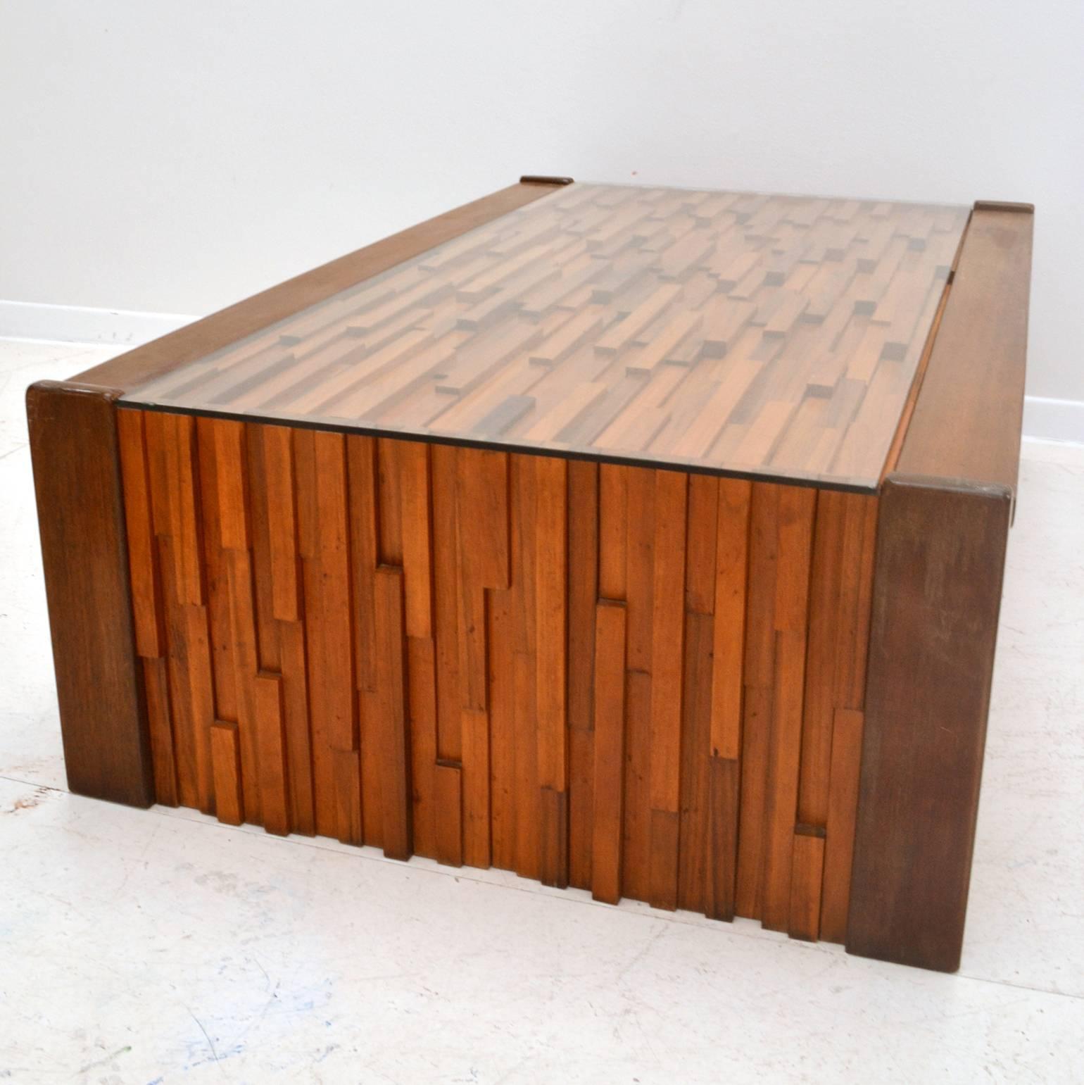 Brazilian coffee table designed as a sculptural relief of various tropical hardwoods in different heights and lengths to create a Brutalist effect edged with Mahogany and fitted glass top. The table is made in Brazil by Percival Lafer. Table and