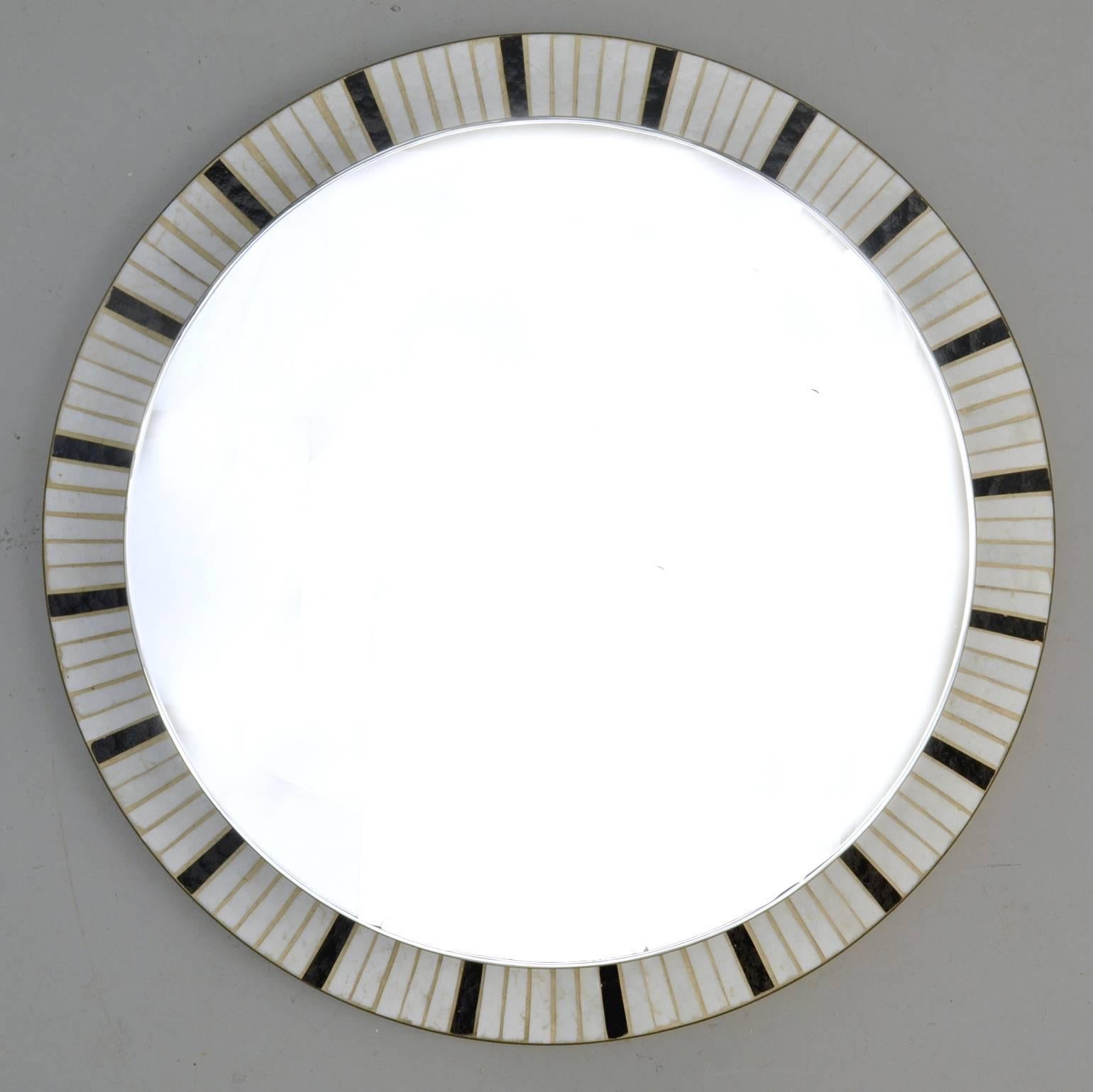 Round illuminated mirror edged with a brass border and inlaid with irradiating black and white glass mosaic.
The mirror is lit with a round fluorescent light fixture that gives a smooth light all around the mirror. This mirror is ideal for a