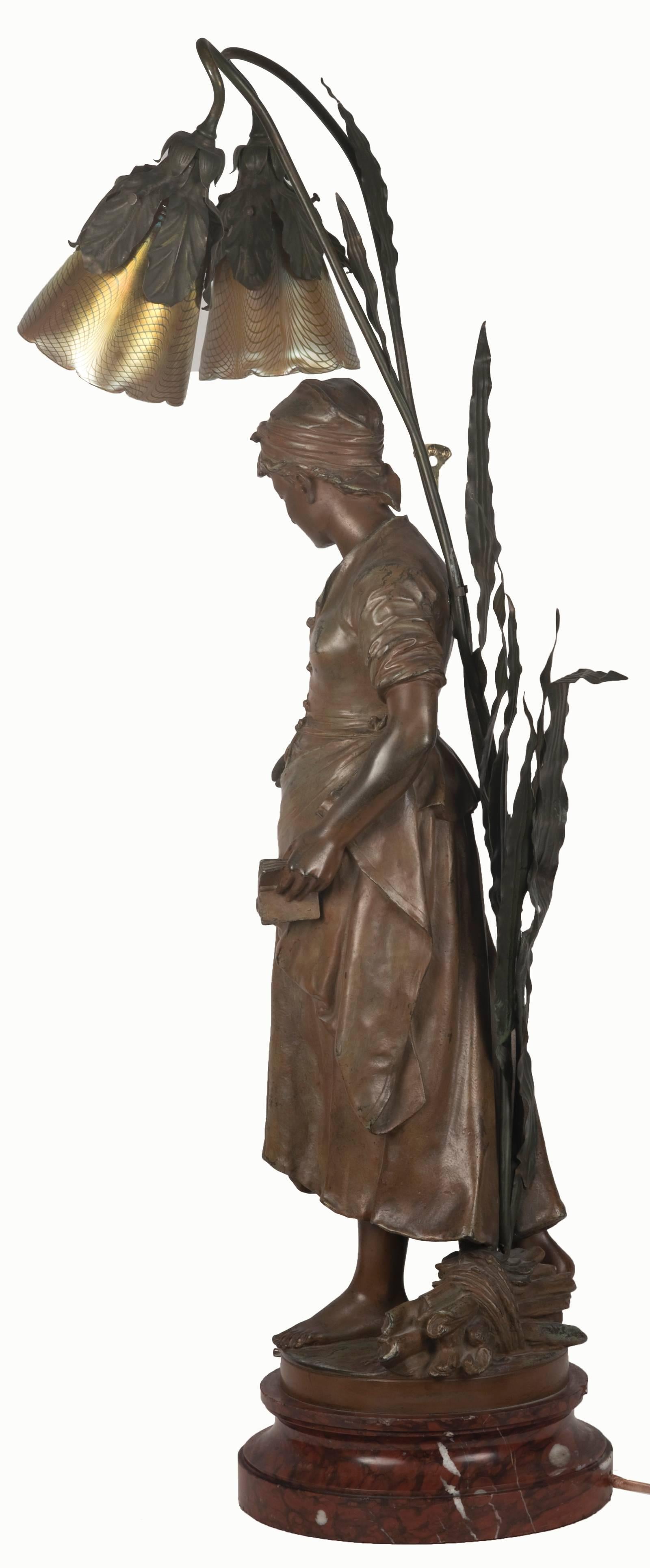 A finely detailed depiction of a female peasant dressed in simple garments, head wrap and apron, holding a small book in one hand while reaching out with the other. A small bushel of sticks sits at her bare feet. The original spelter figure, signed