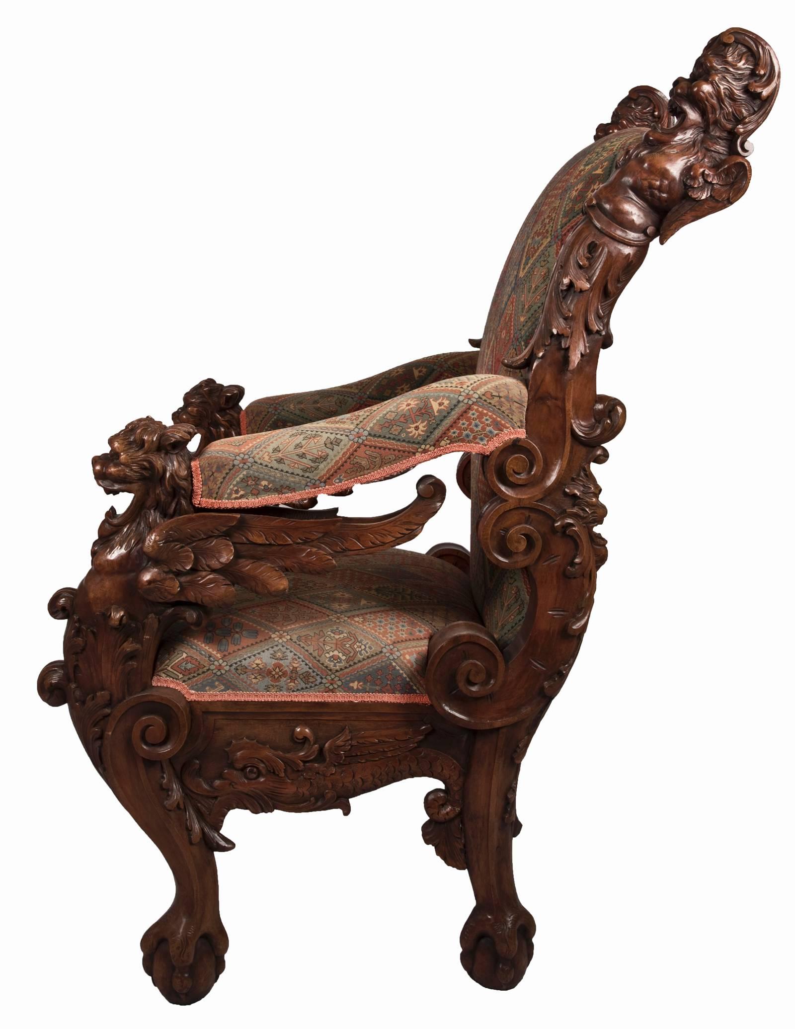 A monumental 19th century German throne chair executed in carved mahogany with upholstered wide seat and high back. This stately chair features carved figural lions at the headrest, deeply carved foliate and C-scroll stiles, with imposing carved