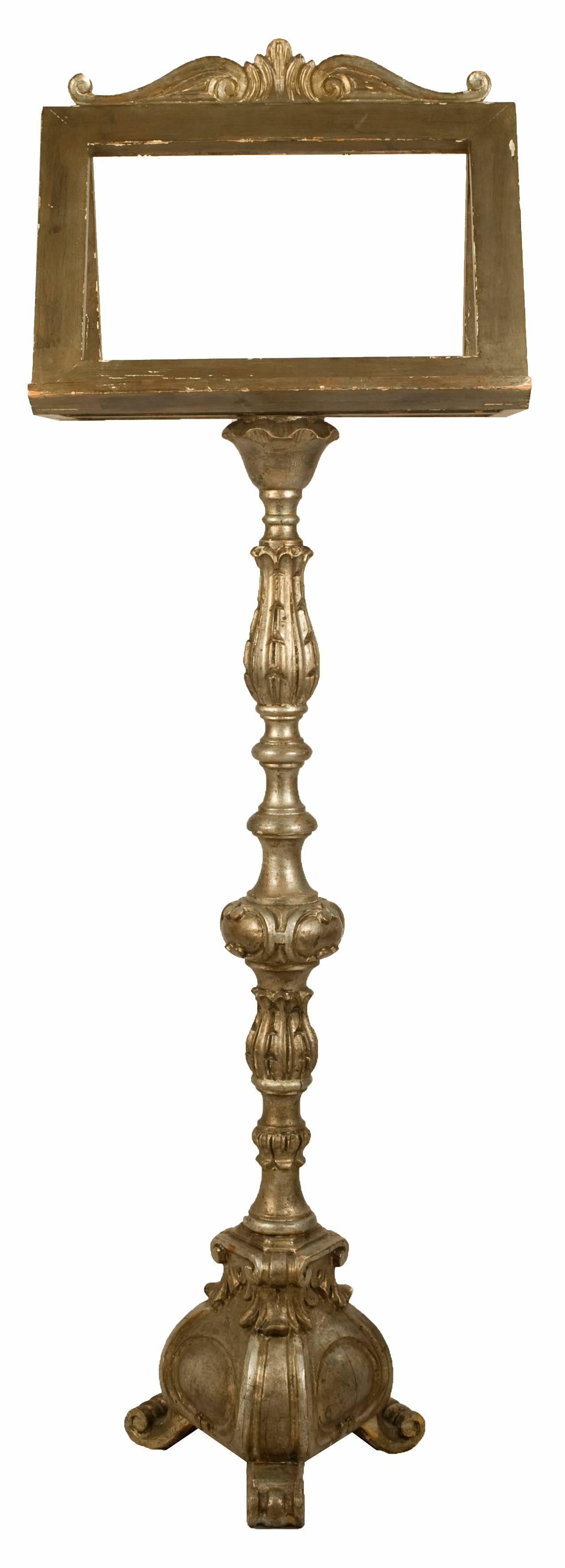 A tall floor music stand or lectern, elegantly carved and detailed. Double-sided lectern topped with simple filigree crest and supported on carved and turned stem, with tripod base ending in scrolled feet.