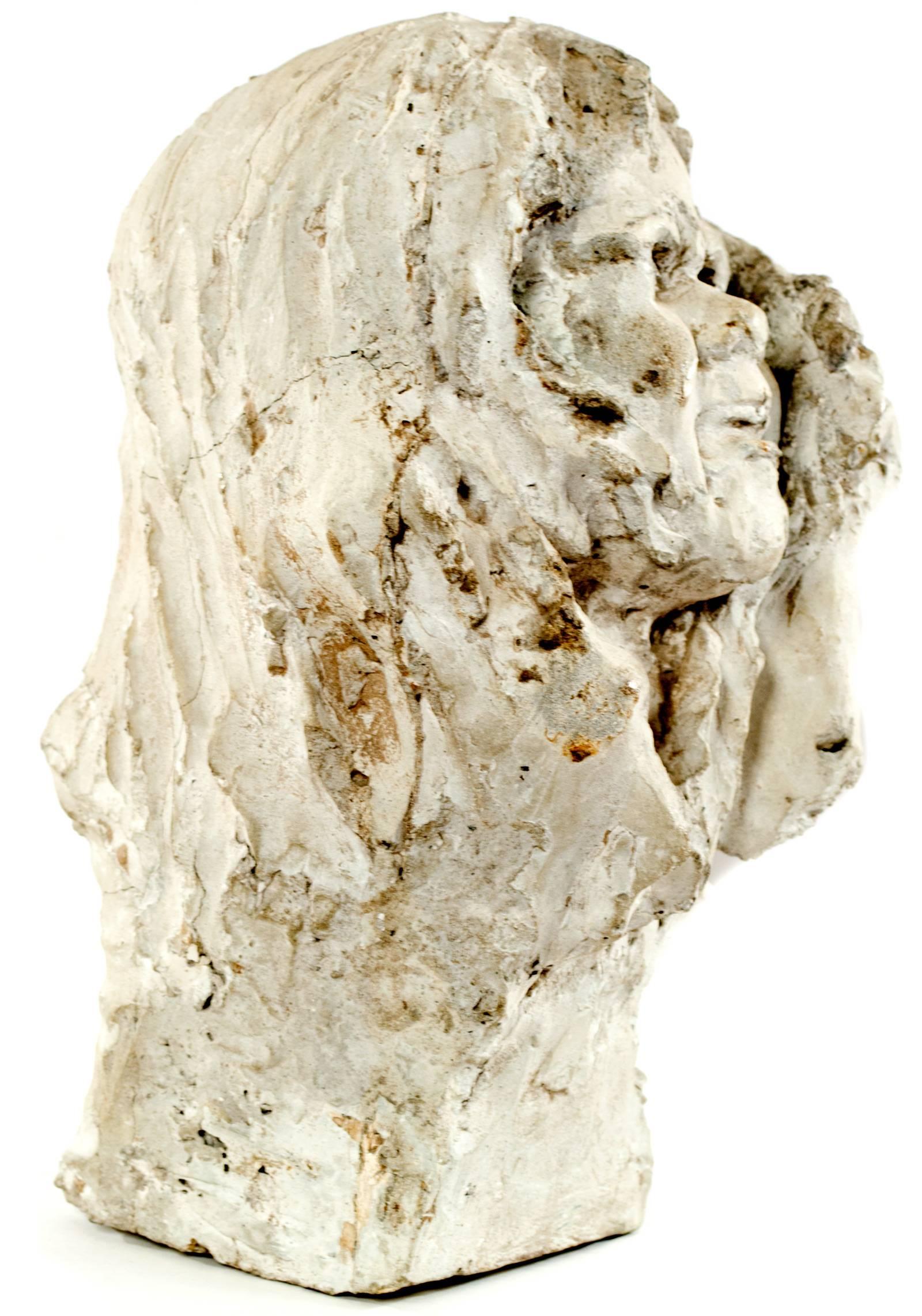 A head emerges from this plaster block study, the left hand, just only discernible, clutches at what would be cloth draped around the figure's head. The back of the draped head is quite rough, the finger markings of the sculptor's hands deep and