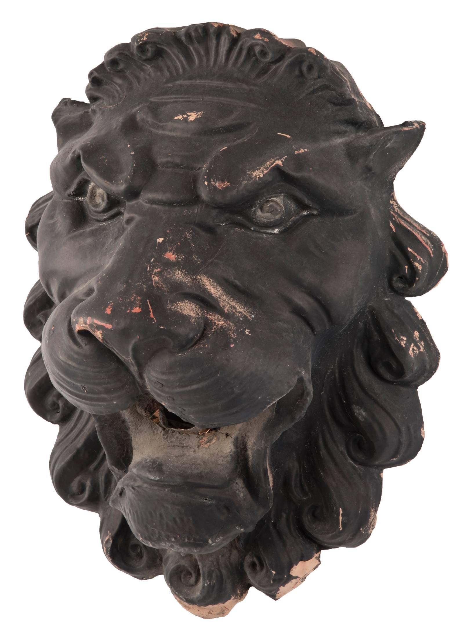 A pair of lion heads in stamped copper with stylized curled mane, pointed ears, and a menacing stare expressed in their eyes. Originally the pair held a chain used to hold an awning along the side of a historical building in Downtown Salt Lake City,