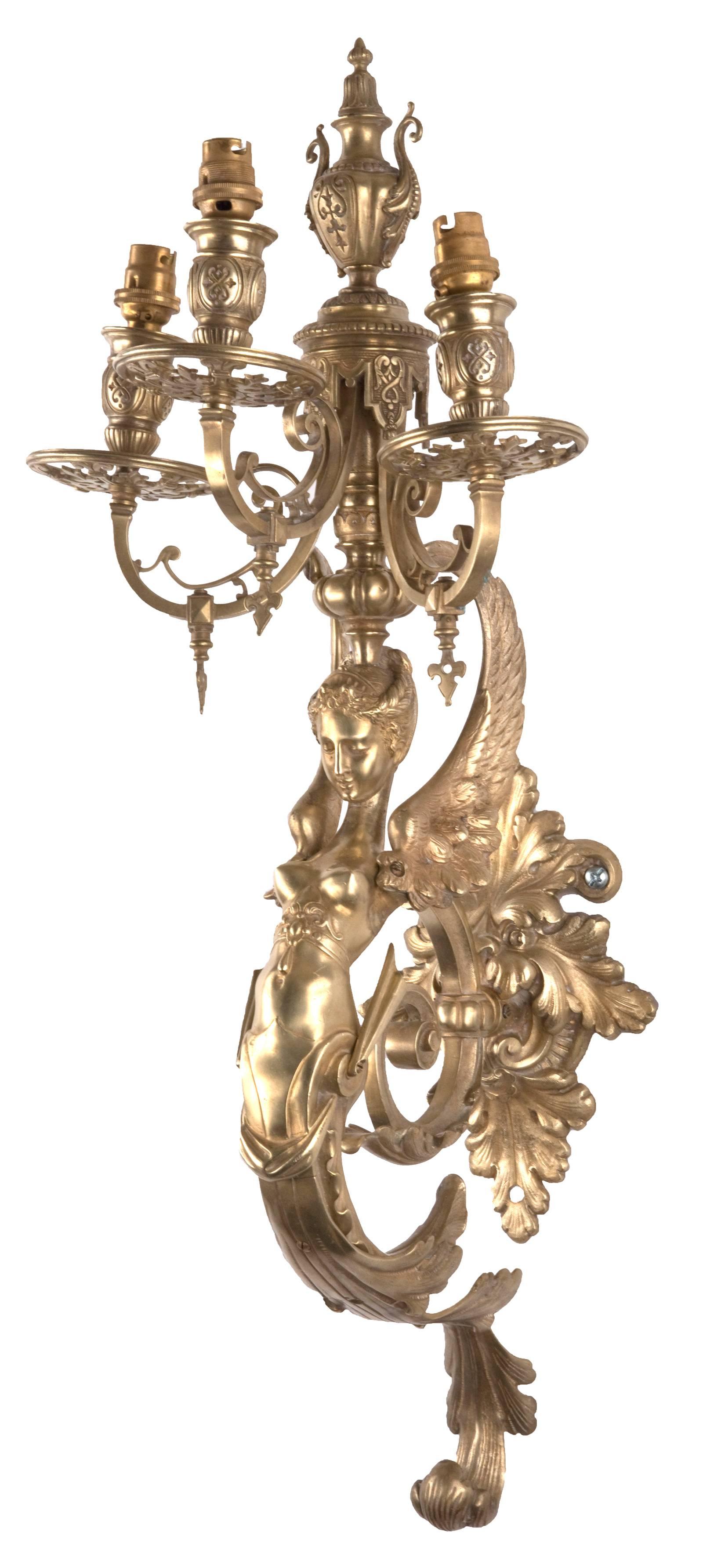 A pair of 19th century hand chased and finely detailed ormolu three-light wall sconces supported by cast, winged caryatids of elongated form, which terminates in stylized filigree.