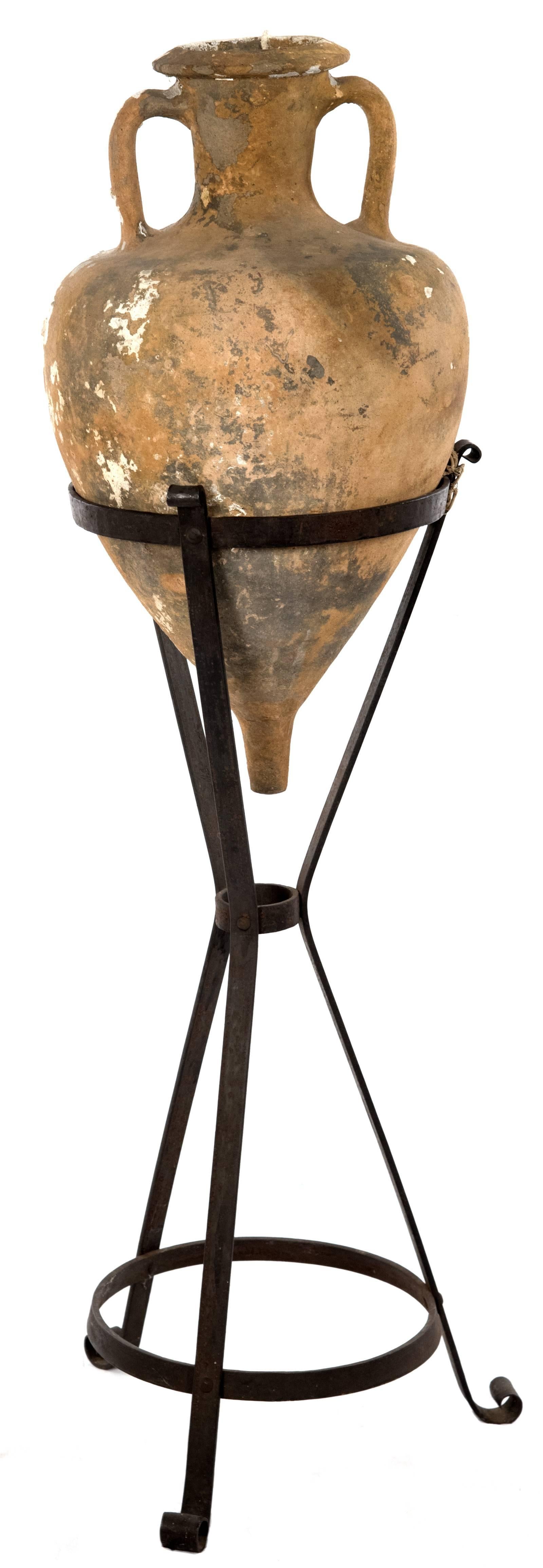 A Greco-Italic terracotta Amphora with cylindrical neck with two side handles, of a globular and V-shaped form with the body tapering into a cylindrical pointed spike at its base. The Amphora is supported on wrought iron conical tripod Stand.

