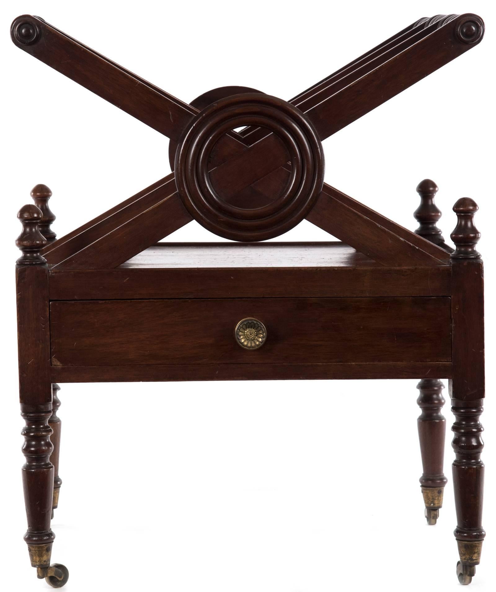 An early 19th century mahogany three division X-frame Canterbury with carved circular decoration and finely turned uniting top rails over a frieze drawer with single brass pull, on turned legs with brass capping’s and castors.