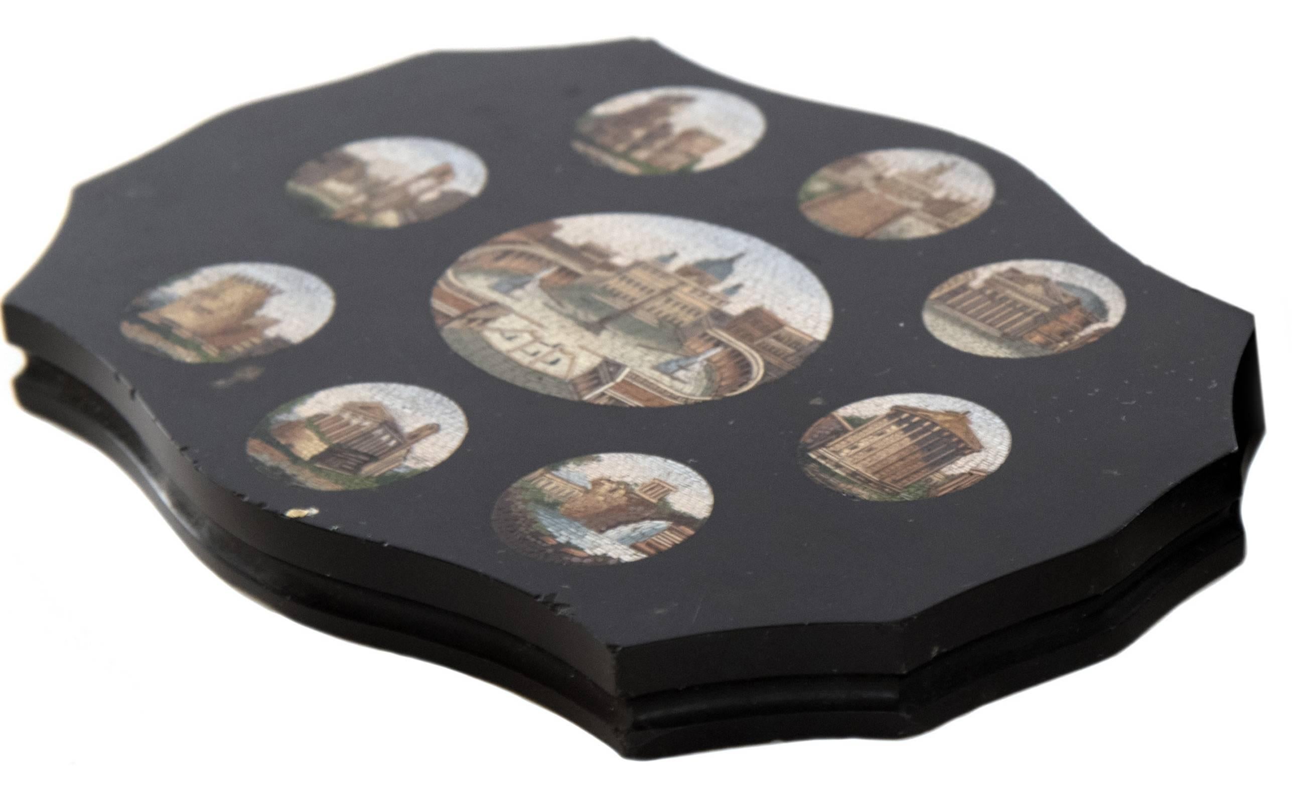 A Grand Tour micromosaic paper weight depicting vignettes of historical Roman architectural landmarks, set within scalloped black marble form. In the centre is a large roundel depicting St. Peter's Basilica, which is surrounded by smaller vignettes