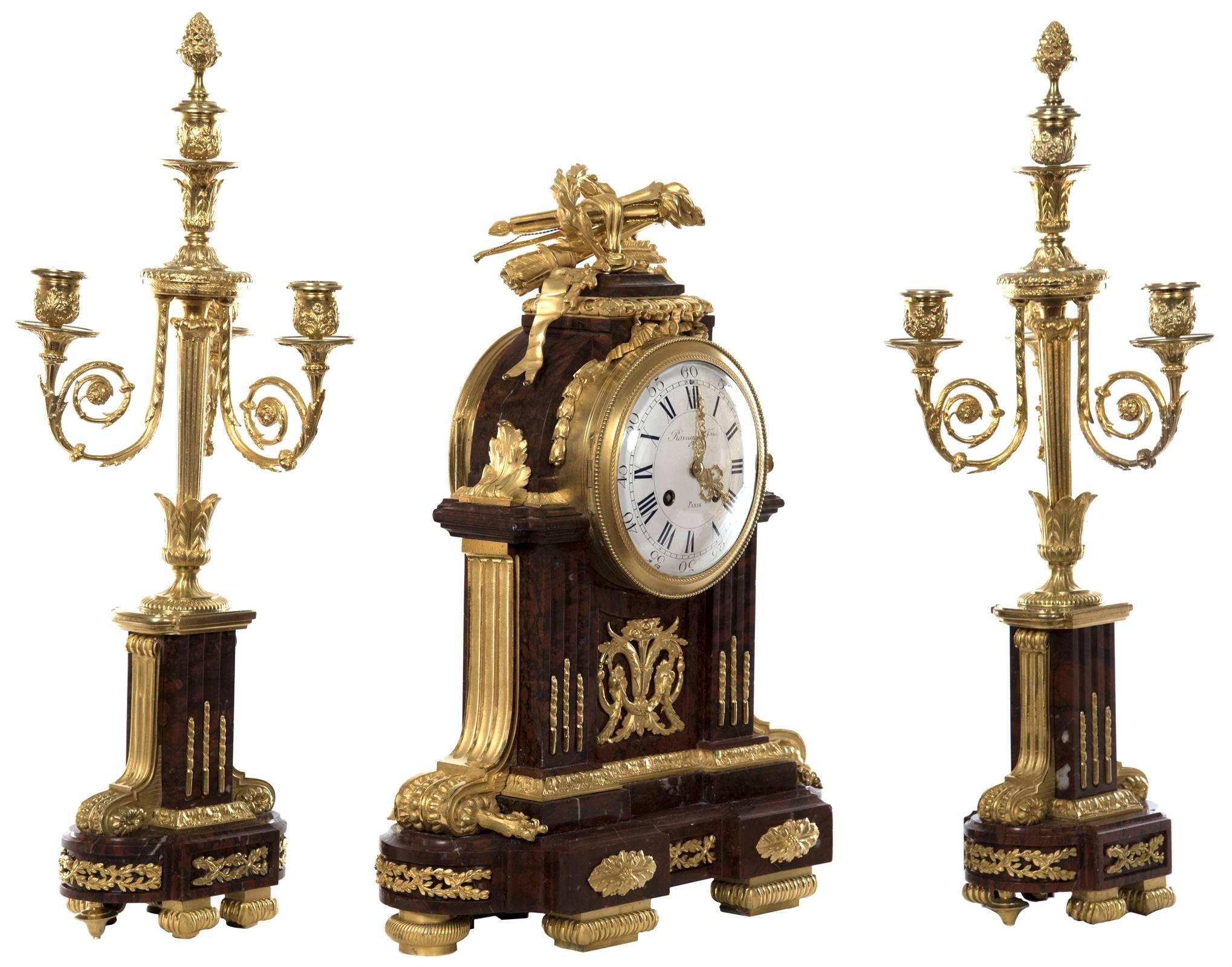 A red griotte marble and ormolu three-piece clock garniture by the clockmaker and bronzier Raingo Frères, dating from the late 19th century, comprising a mantel clock and a pair of four-light candelabra. The clock is of architectural form with