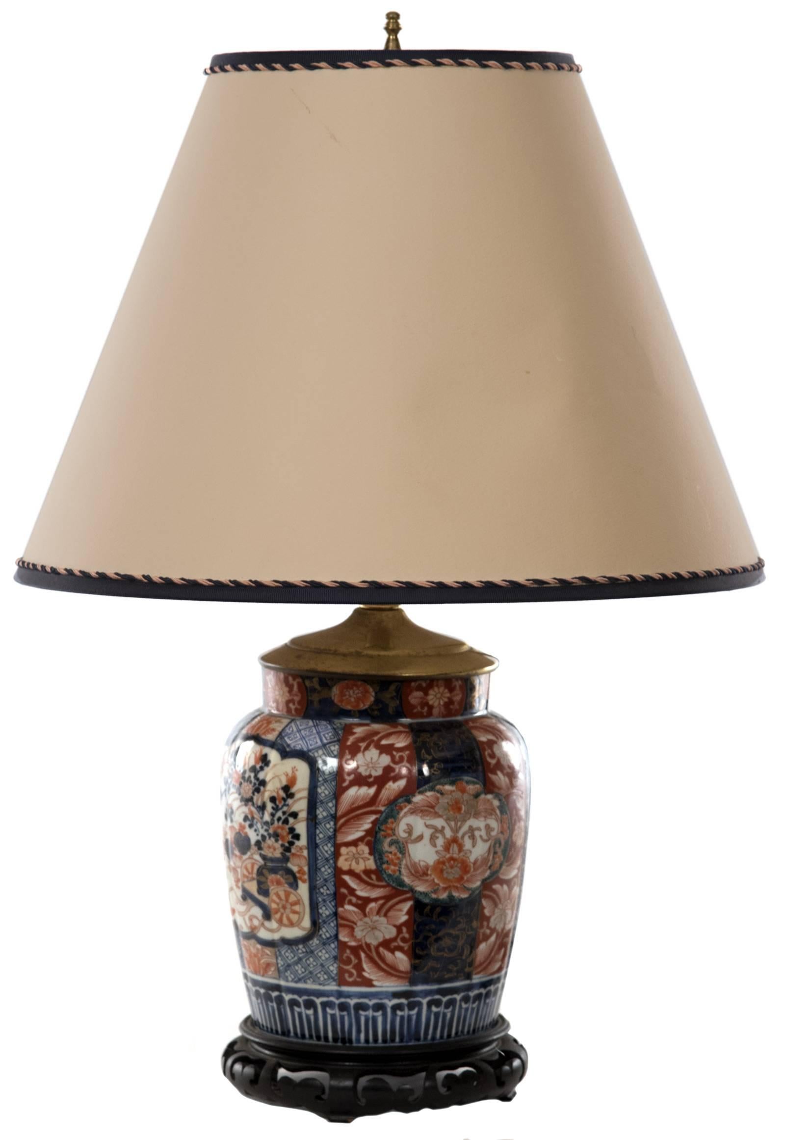 A 19th century Japanese Imari urn of ovoid form on pierced and carved wooden base fitted as a table lamp. The cylindrical neck is decorated with a band of floral motifs on alternating blue and red grounds, surmounting the slightly rounded shouldered