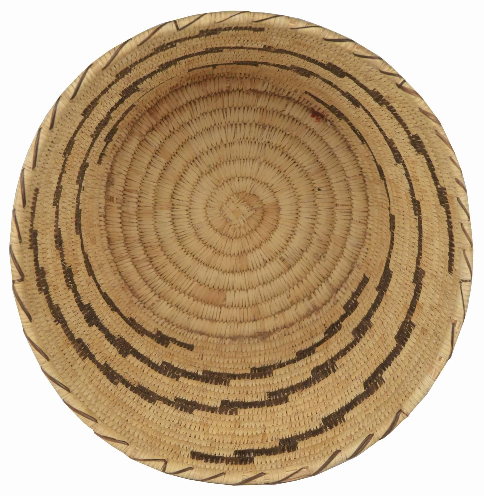 An early 20th century handwoven native American open basket of cylindrical form from the Tohono O’ogham people of southern Arizona, formerly known as the Papago, with coil base and tightly woven body with brown stair-step detailing. Natural fibres