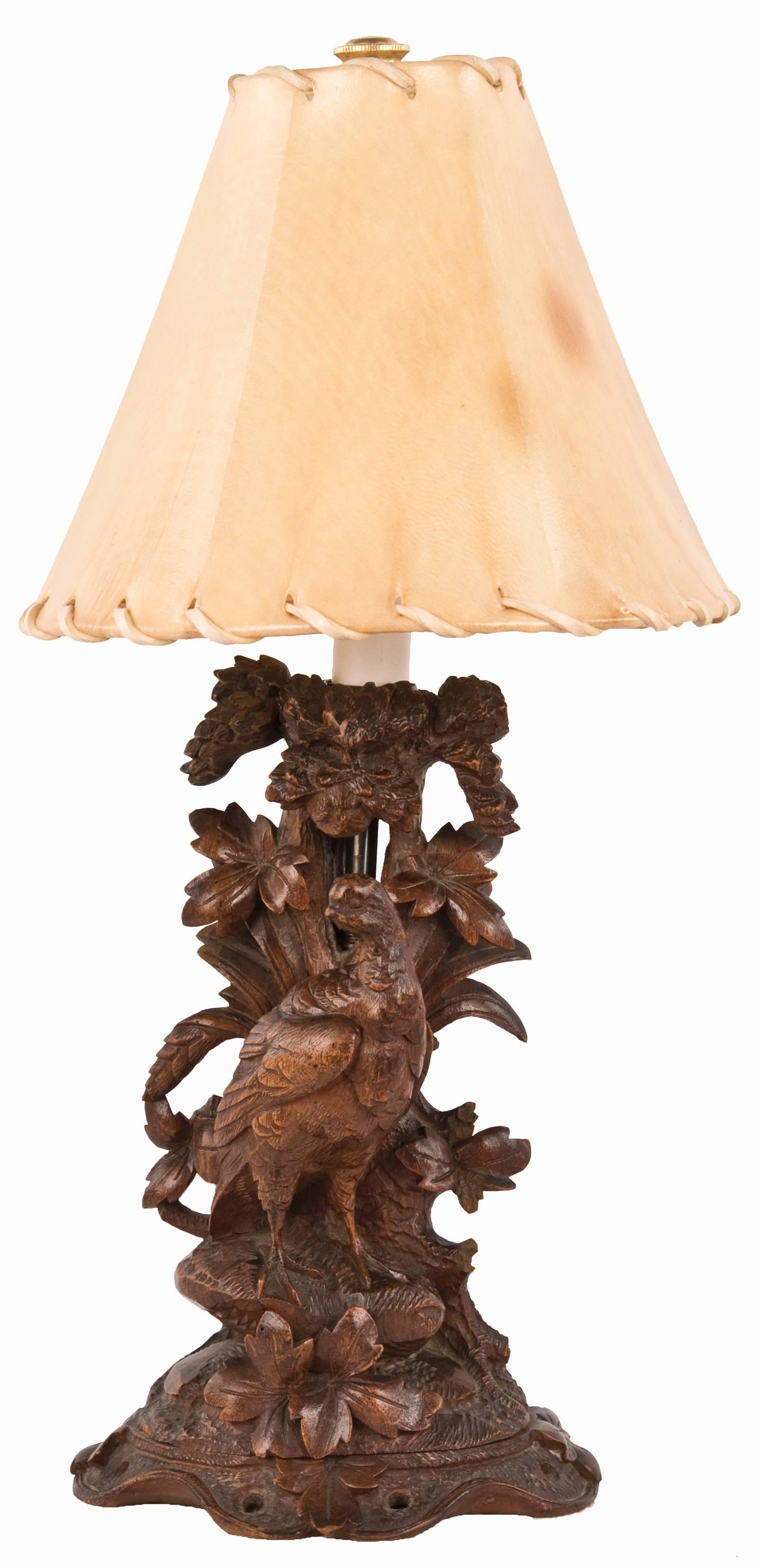 A pair of elaborately carved wood table lamps in the Black Forest style popular in the late 19th century. Opposing pheasants are perched on rocky ground, against a trunk, foliage and pine cones, the figures on a similarly carved base and topped with
