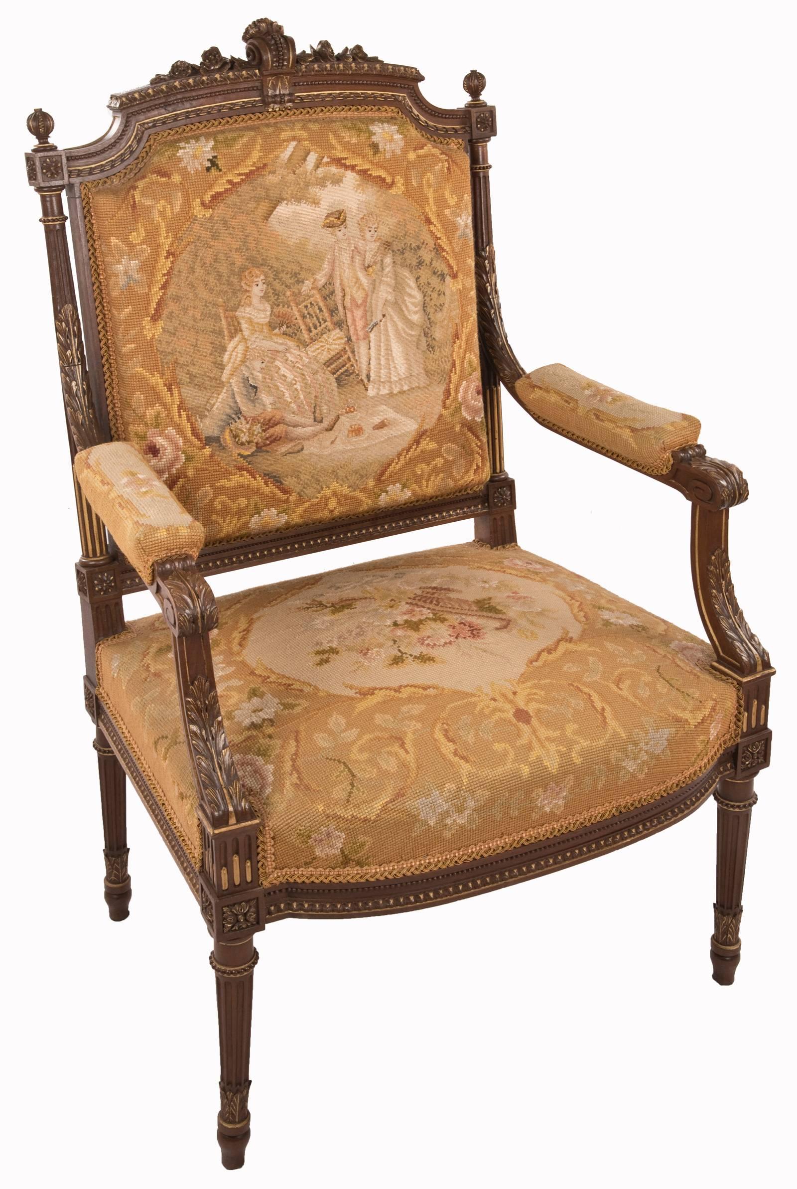 A set of four 19th century Louis XVI style needlepoint-upholstered armchairs made of walnut. A carved scroll and flowers decorate the crest rail of the chair, which is flanked by round finials atop fluted stiles carved with acanthus leaves. The