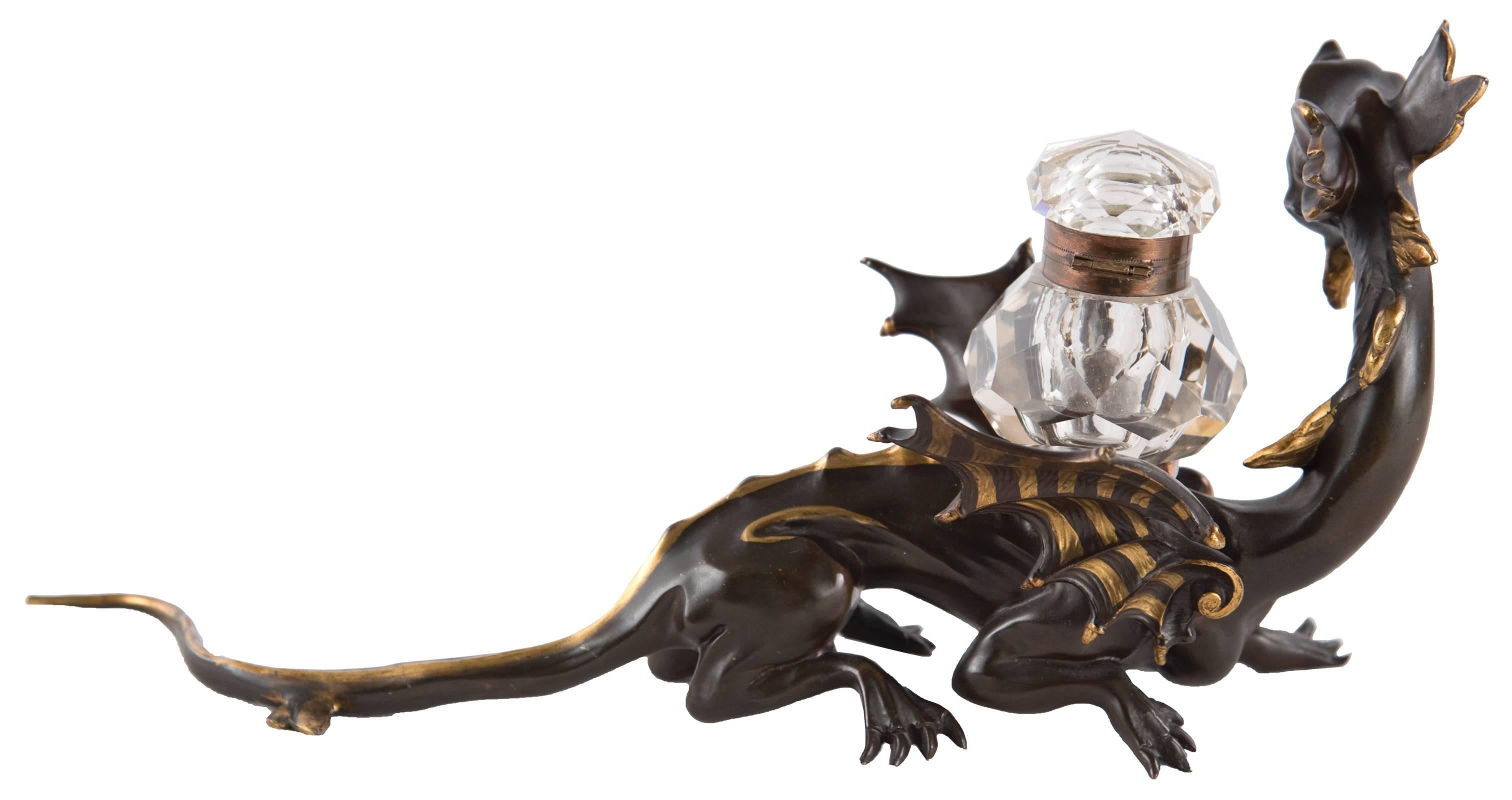 A crystal and brass inkwell with a hinged lid sits on the back of a bronze dragon, which is painted with gold accents. 