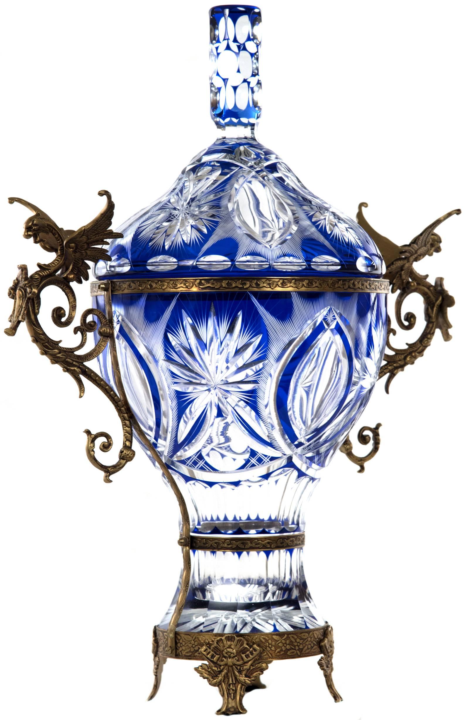 A large 20th century bronze mounted cobalt cut to clear crystal urn having a foliate decorated bronze rim mounted to each side with finely detailed figural Wyvern handles. The body of the urn is cut to depict oval sunbursts and star cut geometric