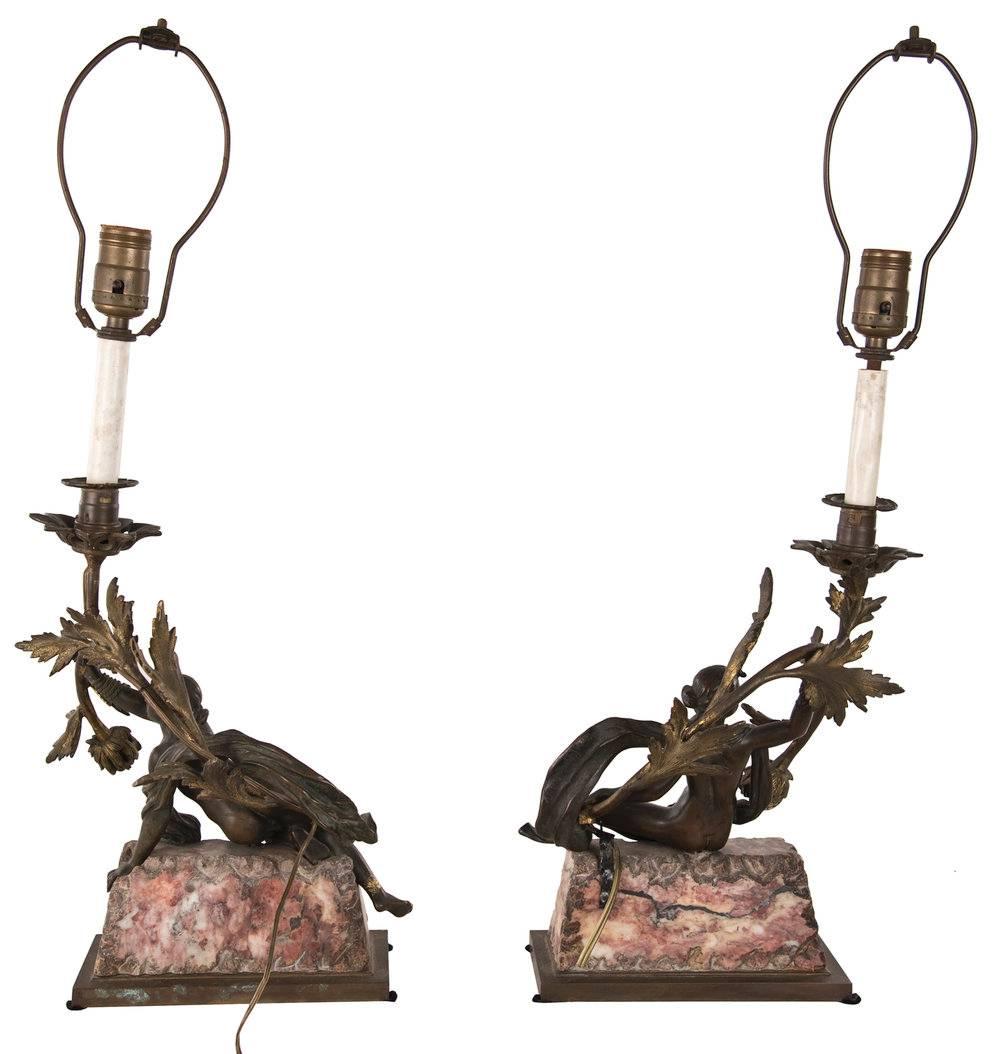A pair of neoclassical candelabra that have been electrified and fitted as table lamps. Each lamp is formed with a gilt bronze female figure sitting on a marble plinth and bronze base with outstretched arms that clasp a large floral stem, which