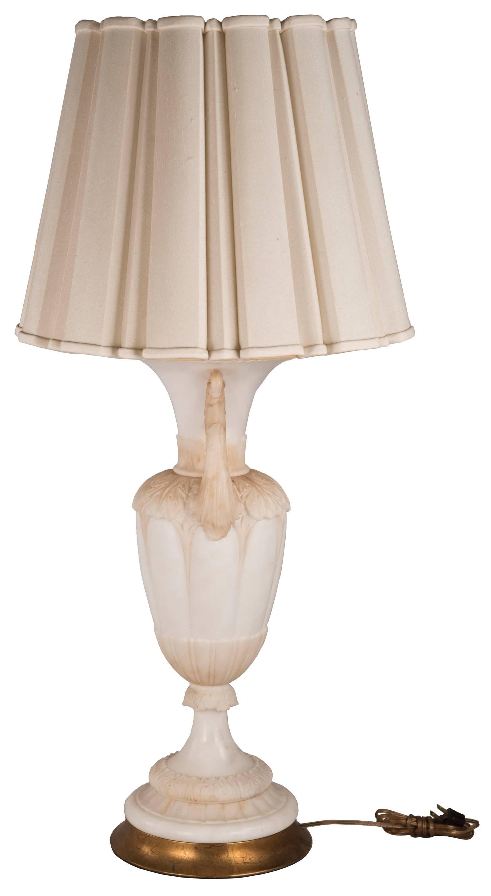 A neoclassical carved alabaster urn table lamp with scrolling foliate handles, with trumpet neck tapering to carved foliate banded collar above acanthus leaf carved shoulders and fluted body, on socle with high-relief acanthus leaf collar over