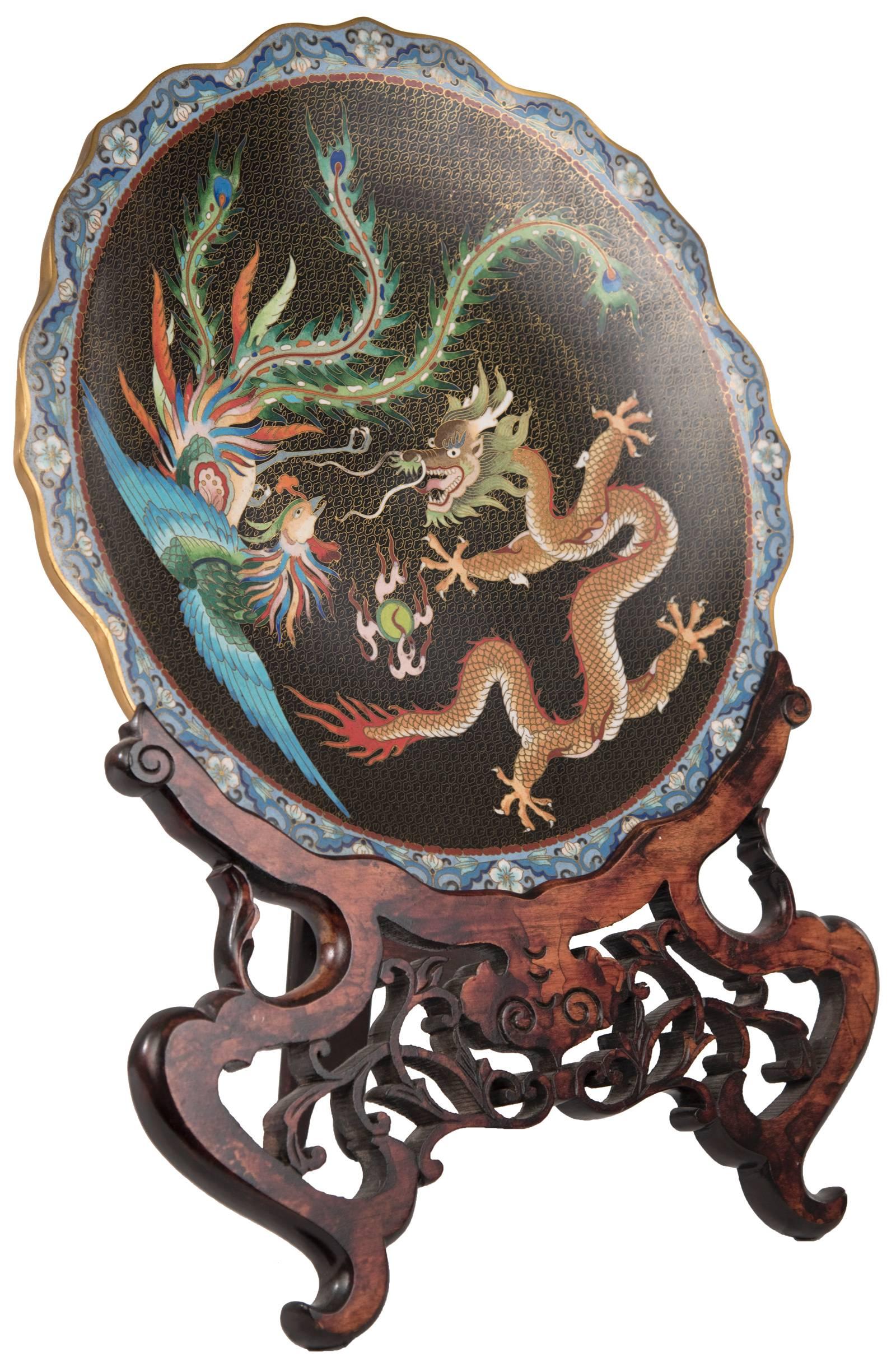 A beautiful Chinese cloisonné enamel plate with shaped petaled edge with a stylized decorated rim that borders the black-ground central medallion, upon which is a brightly decorated phoenix and dragon in flight amongst gilt-painted clouds contesting