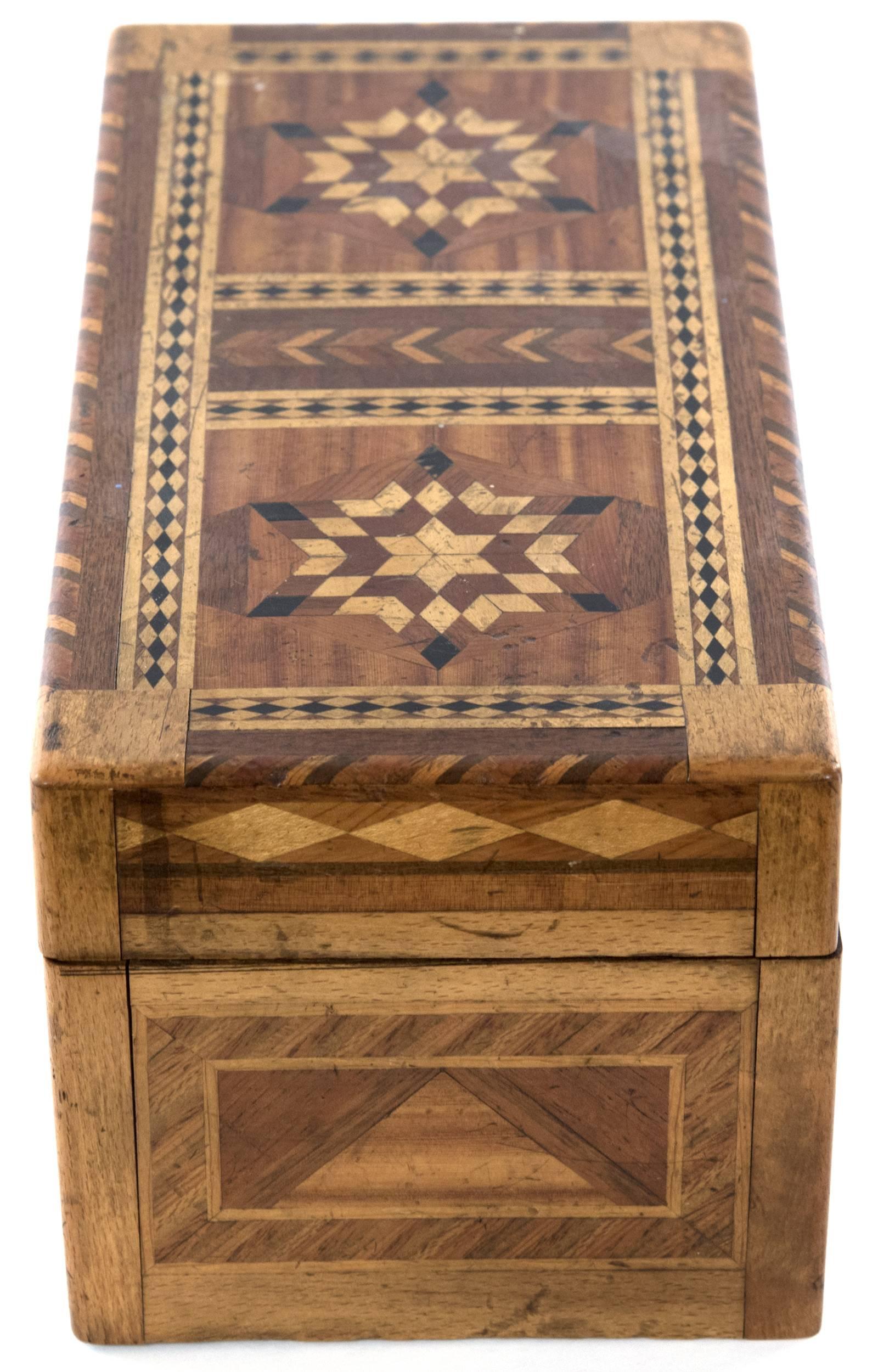 A hinged-lid box with contrasting parquetry inlaid design of light and dark woods in geometric panels and banding, with two six-point stars on the lid. The interior compartment is lined with purple fabric, and the base is lined with parchment