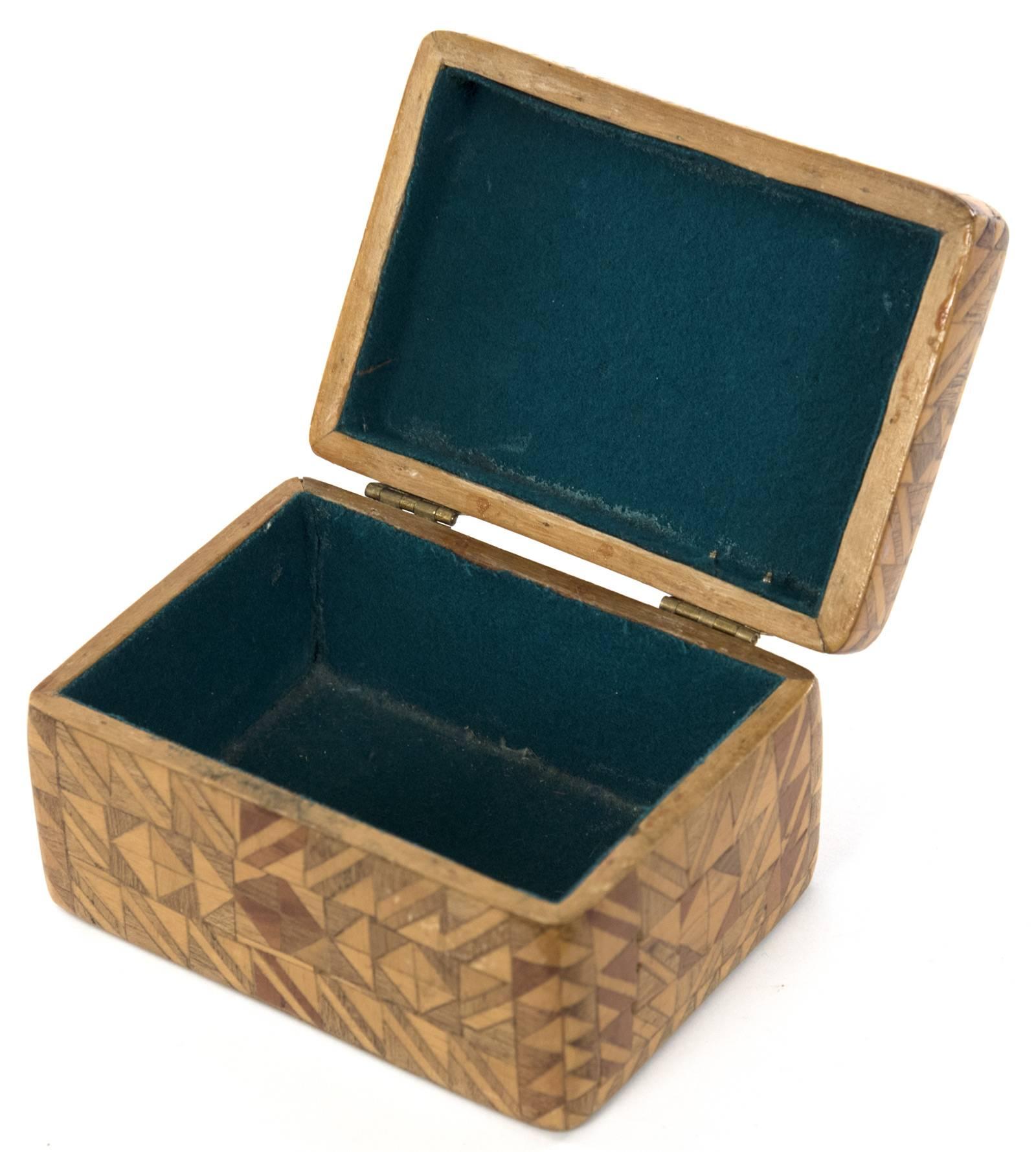 A decorative box with hinged lid, entirely covered with a veneer of several contrasting types of wood in a geometric parquet design comprised of squares, triangles and lozenges. Interior of box is a single compartment lined with green felt. Base of