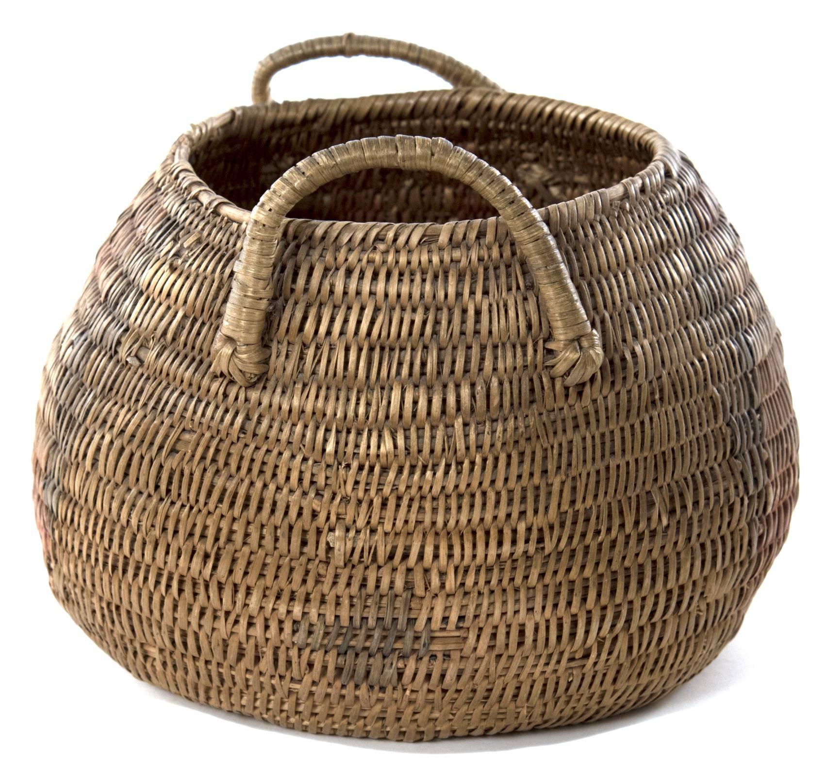 A Native American basket of squat and globular form, with a twined woven body decorated with black red designs and coiled handles raised from the shoulders.