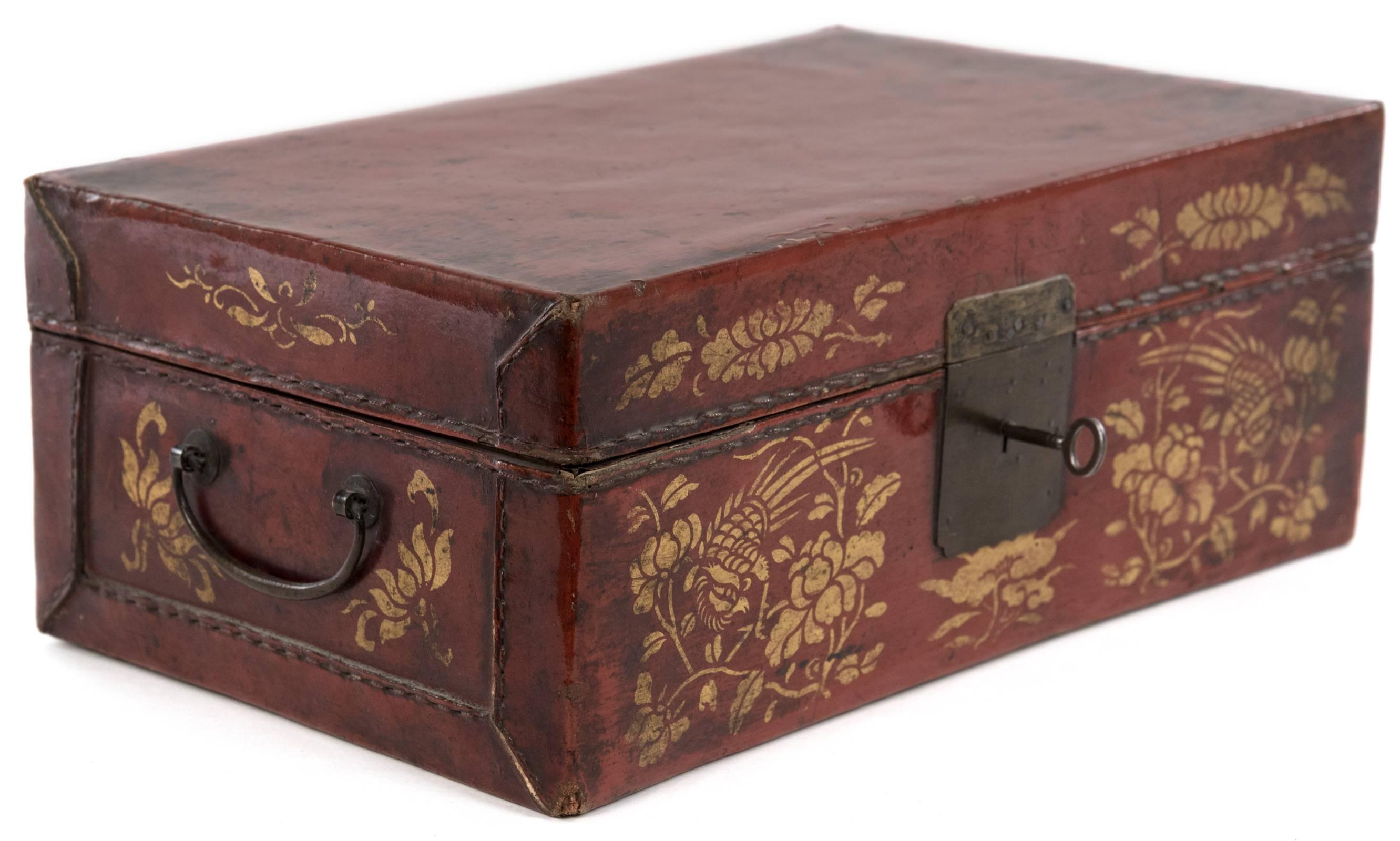A Chinese stitched red leather box with hinged lid, applied painted distress marks and gold-stamped foliate ornamentation; brass handles and lock plate with key. Interior is comprised of one large compartment that is lined with white material.
