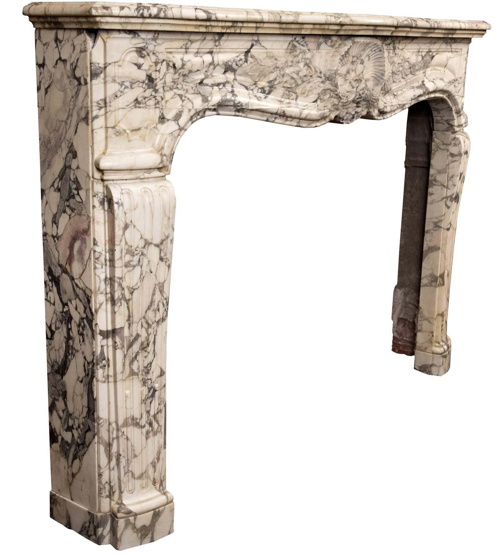 A finely-carved 19th century French cheminée patterned after the early 18th century Régence style, in the rare marble from Lucca, Italy, Brèche Médicis. The central decoration is comprised of an intricately-carved coquille shell flanked by laurel