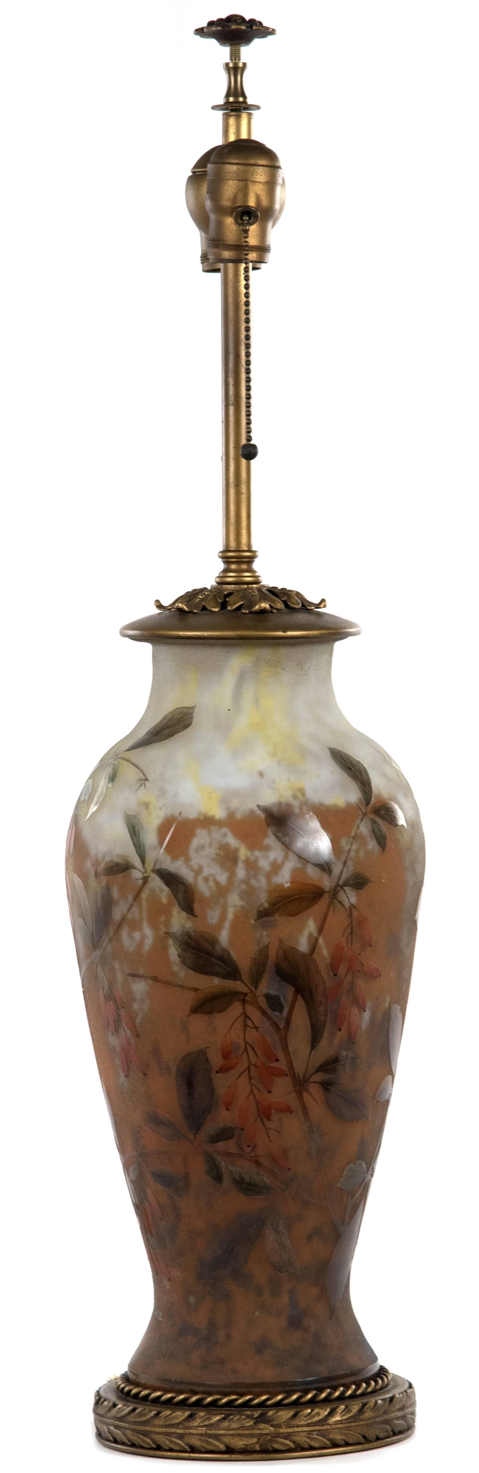 An early 20th century two-light table lamp of baluster form from the French glass manufacturer, Daum. An iridescent enamel of creams and yellows covers the neck and shoulders of the baluster shaped body, transitioning into an earthy-orange. The form