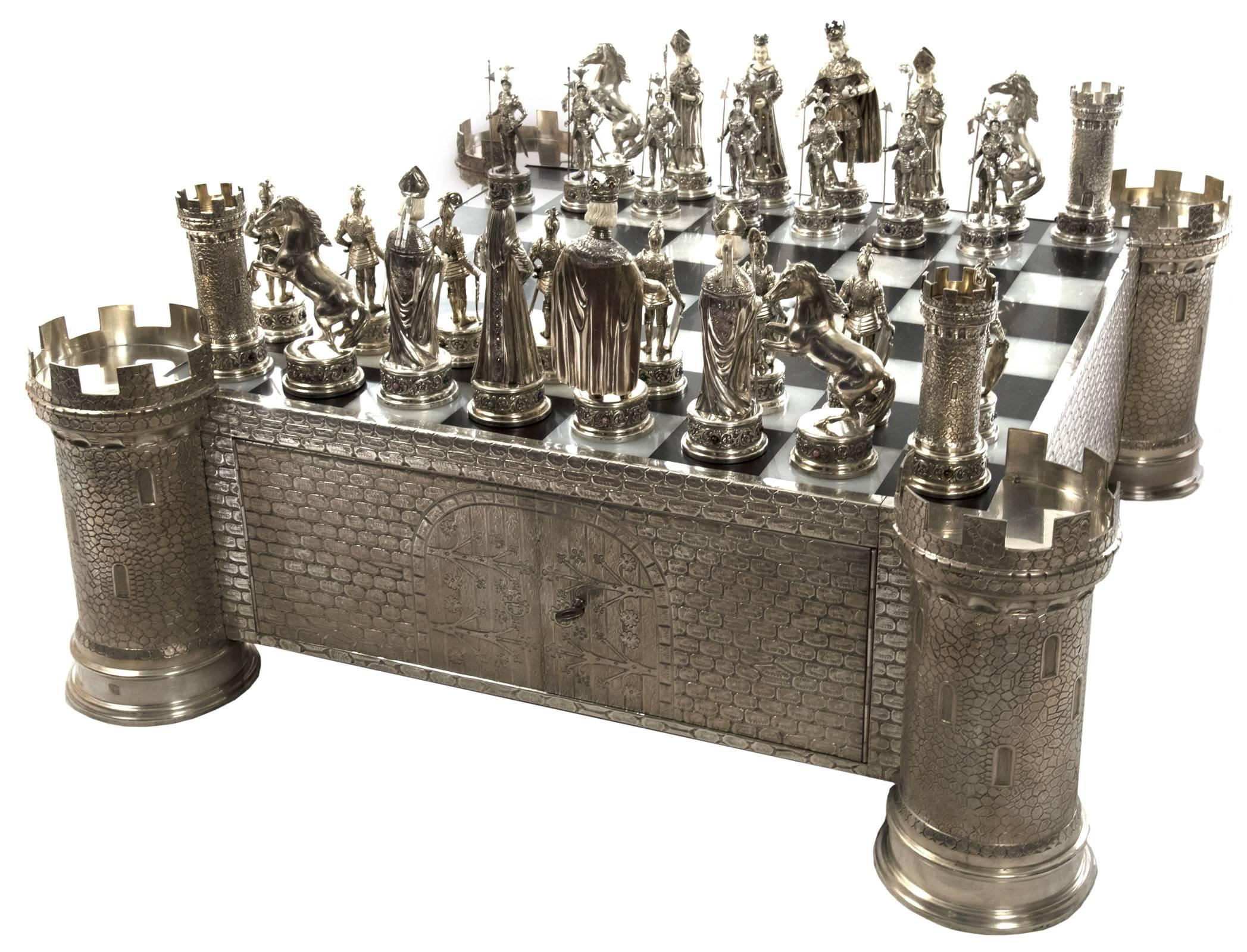 The black and white marble chessboard encased within a silver turreted castle base with crenellated towers at the four corners and chased ashlar block detailing, two locking doors on the front opening to reveal two sliding fitted wooden drawers