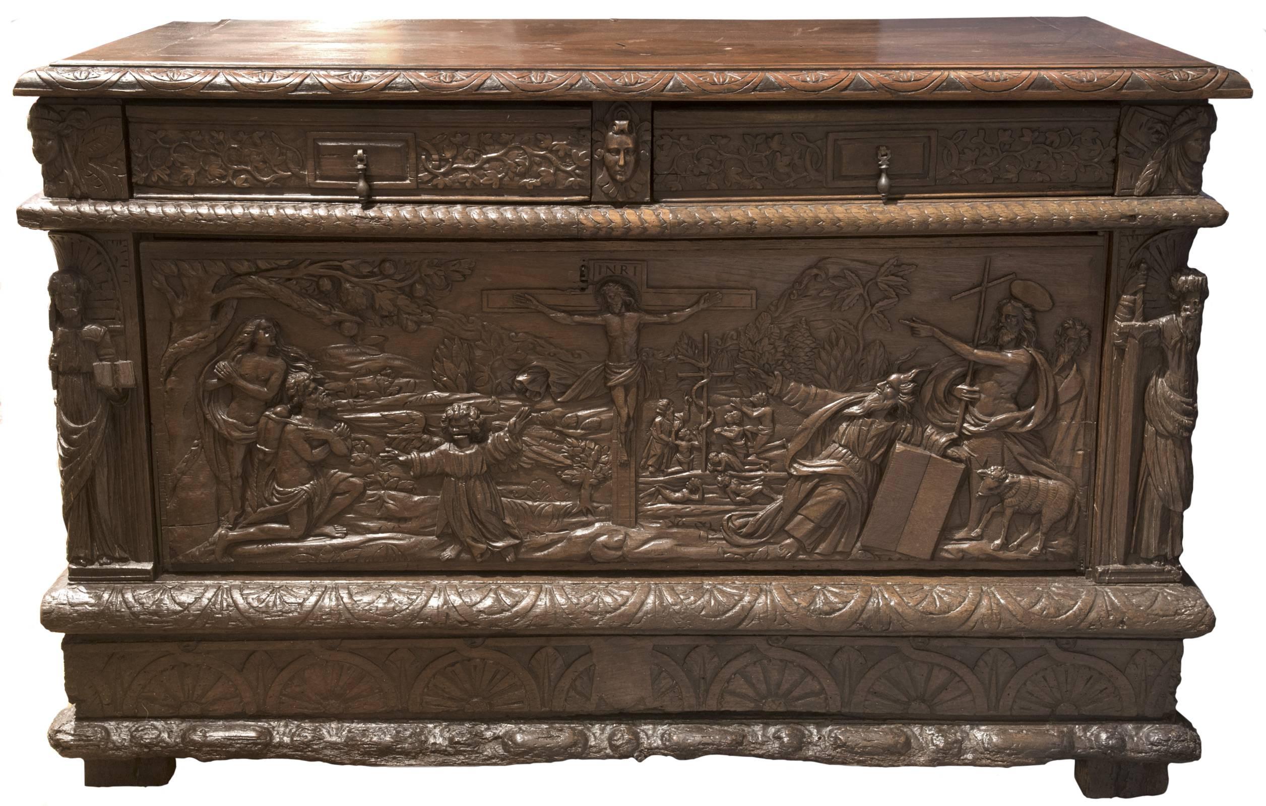 A Renaissance style hand-carved oak sideboard with two drawers with carved pulls and carved foliate motif, that sit above a single removal panel depicting a relief carving with a centre image of Christ on the cross, which is flanked with depictions
