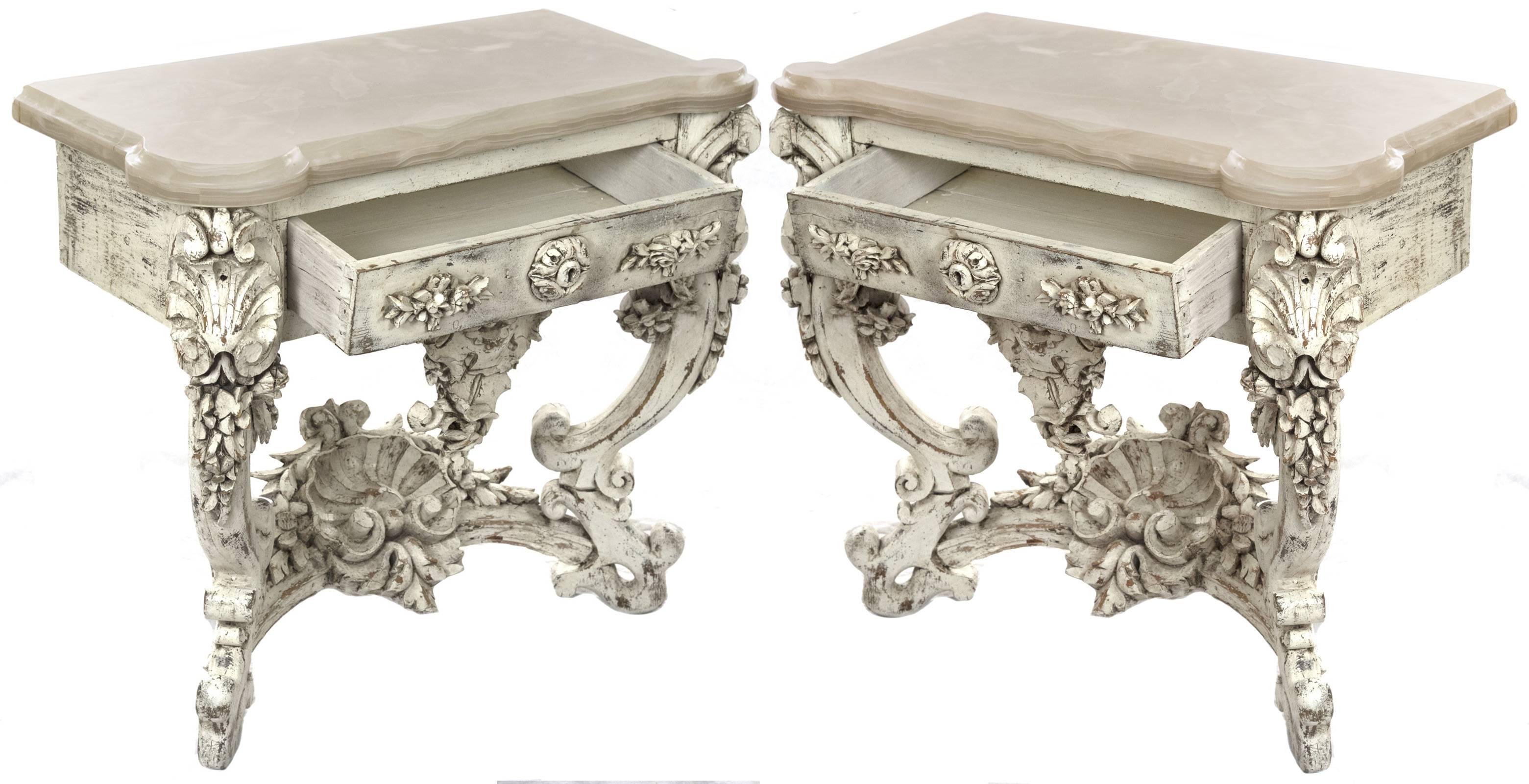 An elegant pair of early 19th century Louis XV style end tables hand-carved from solidwood and painted white. Each piece is raised on square feet and supported on scrolled legs with impressive rich floral carvings, connected by a conforming