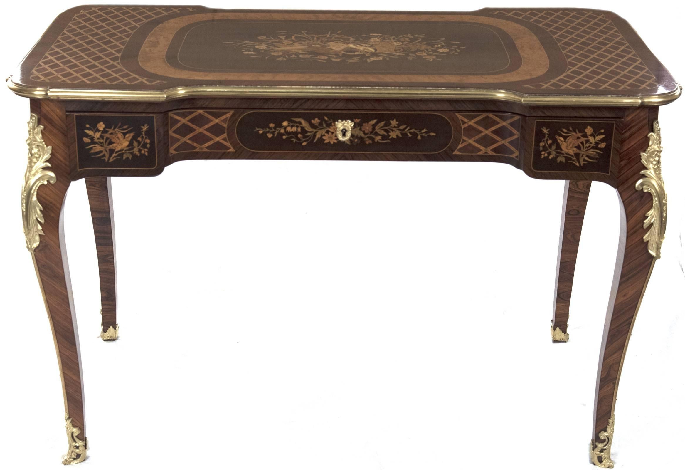 A handsome Louis XV style writing desk having a shaped top with a central ebonized ground inland with marquetry of musical instruments and scrolling florals surrounded by contrasting bands of inlay, which are flanked by trellis patterned marquetry