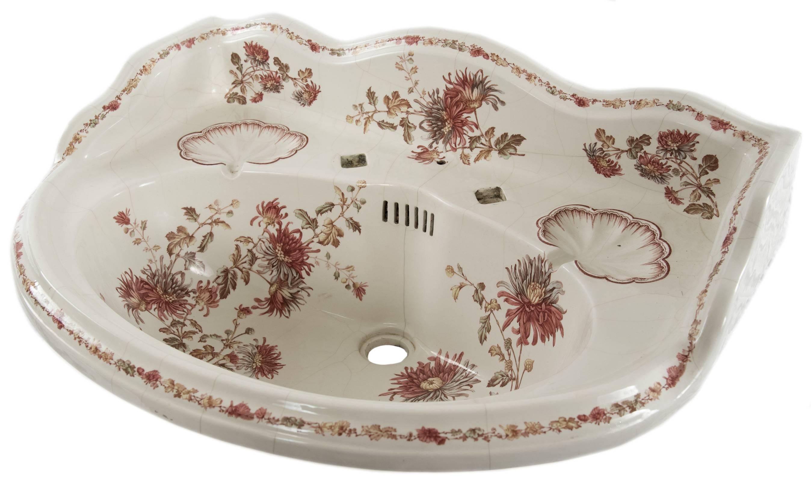A Victorian porcelain basin with an under glaze polychromatic transfer design of garland and florals, the shaped edges trimmed in a chain of small flowers. There are two soap dishes with raised detail above the oval bowl. The sink is drilled for hot