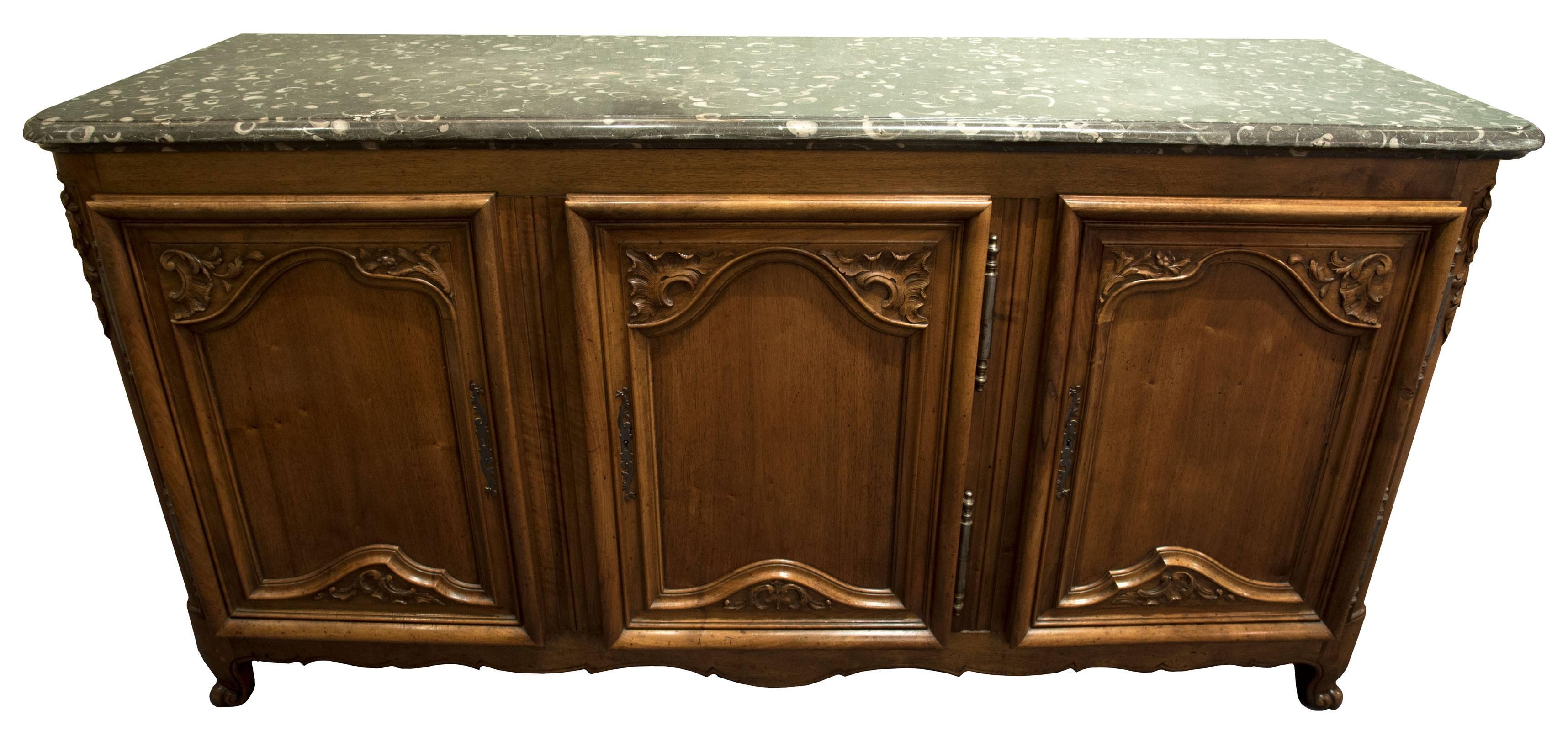 A walnut sideboard with green marble top with a moulded edge above three cabinet doors with silver self-mortised hinges and the door fronts decorated with carved relief details in the corners. The sides are carved with a simple panel form and are