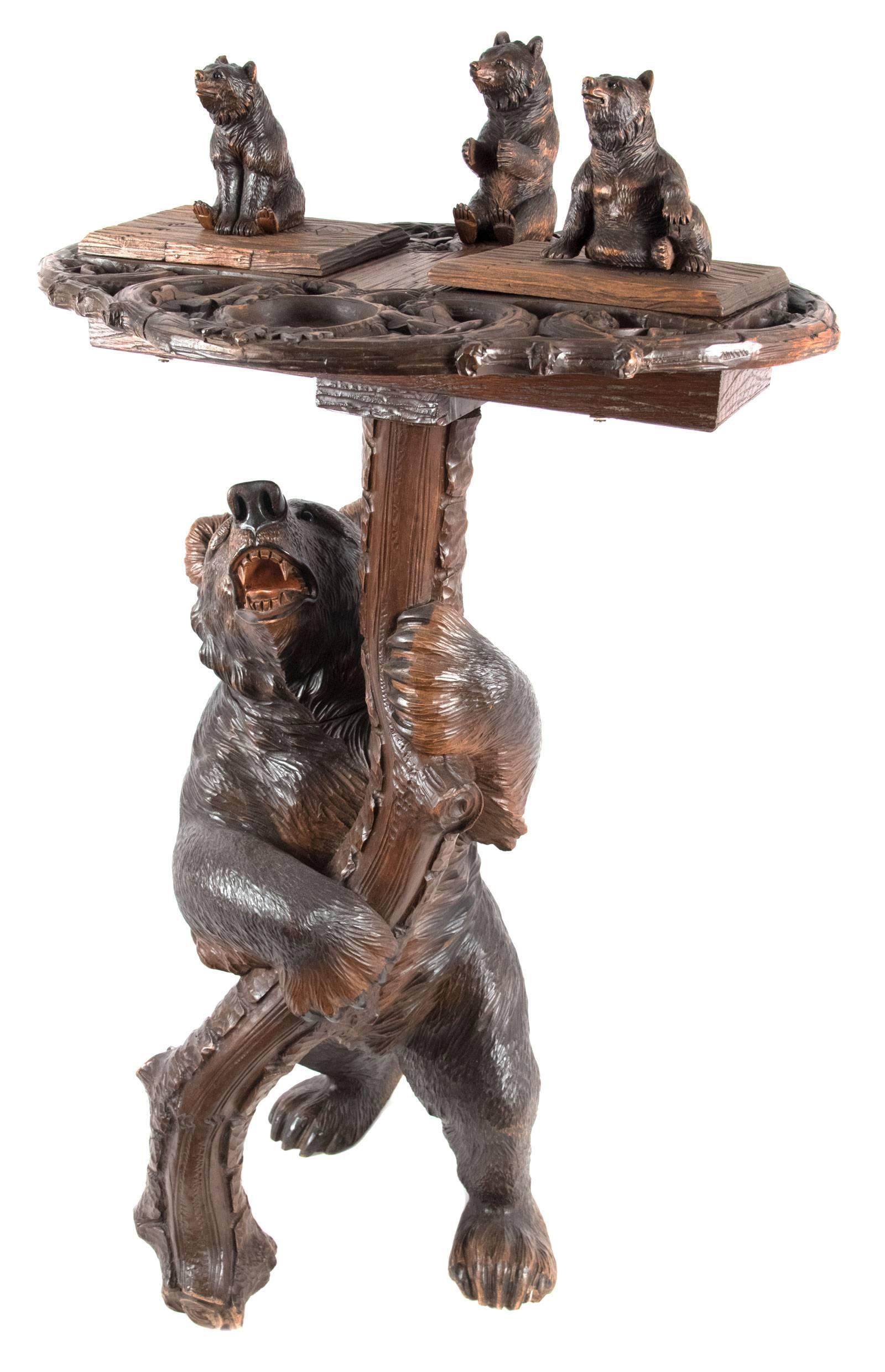A well carved Black Forest oak smoking stand featuring a large carved bear standing upright at the base of a naturalistic tree that is supporting a stylized tray with three small bears, two of which sit on lids that open to reveal a storage