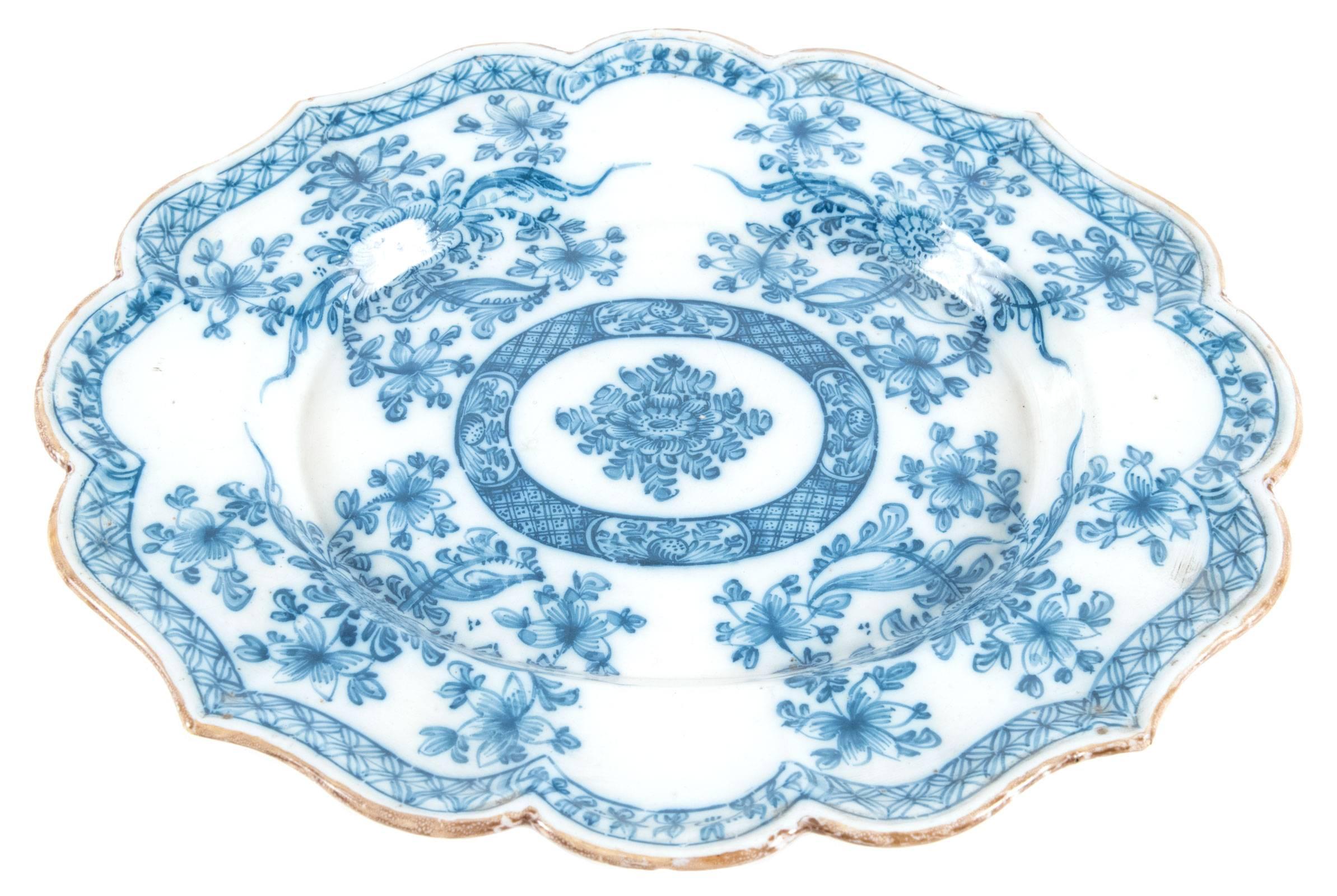 A beautiful blue and white Chinese porcelain lotus shaped plate trimmed with gilt enamel. The face is hand-painted with stylized border that follows the shape of the plate and encompasses four groupings of flowing floral and foliate designs, which