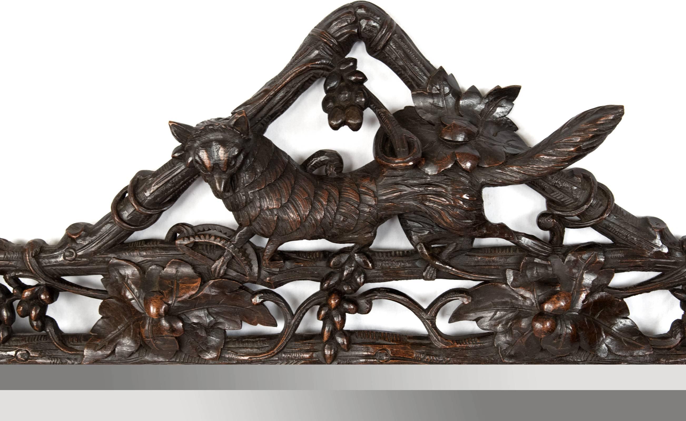 A hand-carved oak Black Forest mirror from the last quarter of the 19th century with a frame of carved twisting branches, leaves and foliage, crested with the form of an elongated fox.