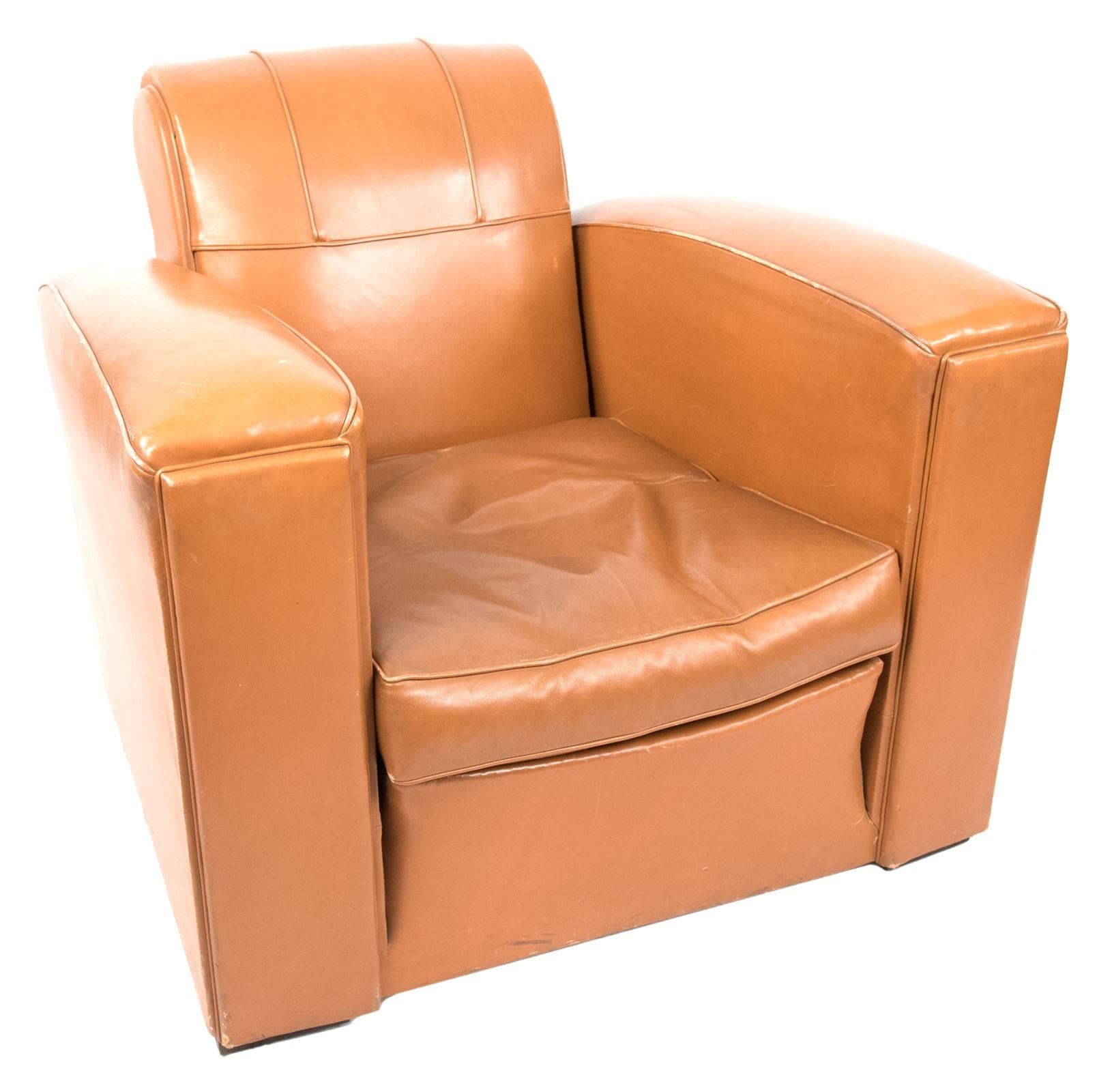 A pair of Art Deco-style leather armchairs with a rolled headrest and oversized armrests, detailed with simple trimming and raised on square wooden feet.