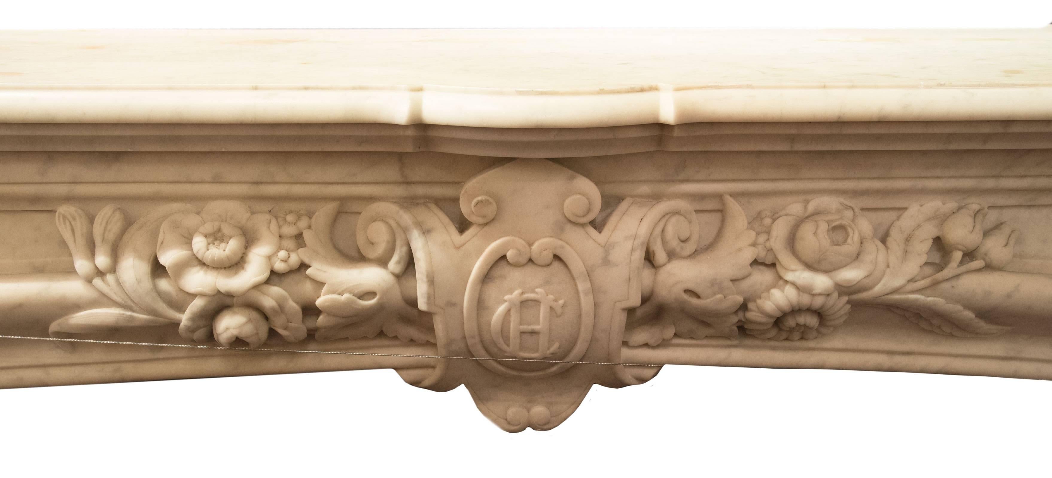 A handsome Louis XVI-style grey-marbled white Carrara fireplace surround with a shaped mantel above a frieze with carved central shield depicting the insignia 