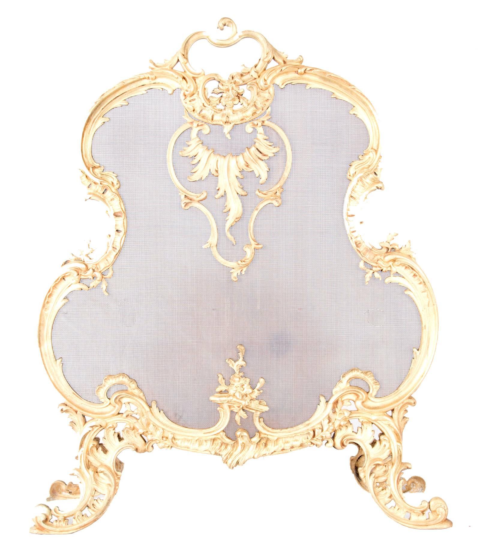 A French gilt-brass Rococo-style fireplace screen, the frame with scrolling foliage and filigree designs and the screen with an acanthus leaf cartouche, raised on scrolled and pierced legs.