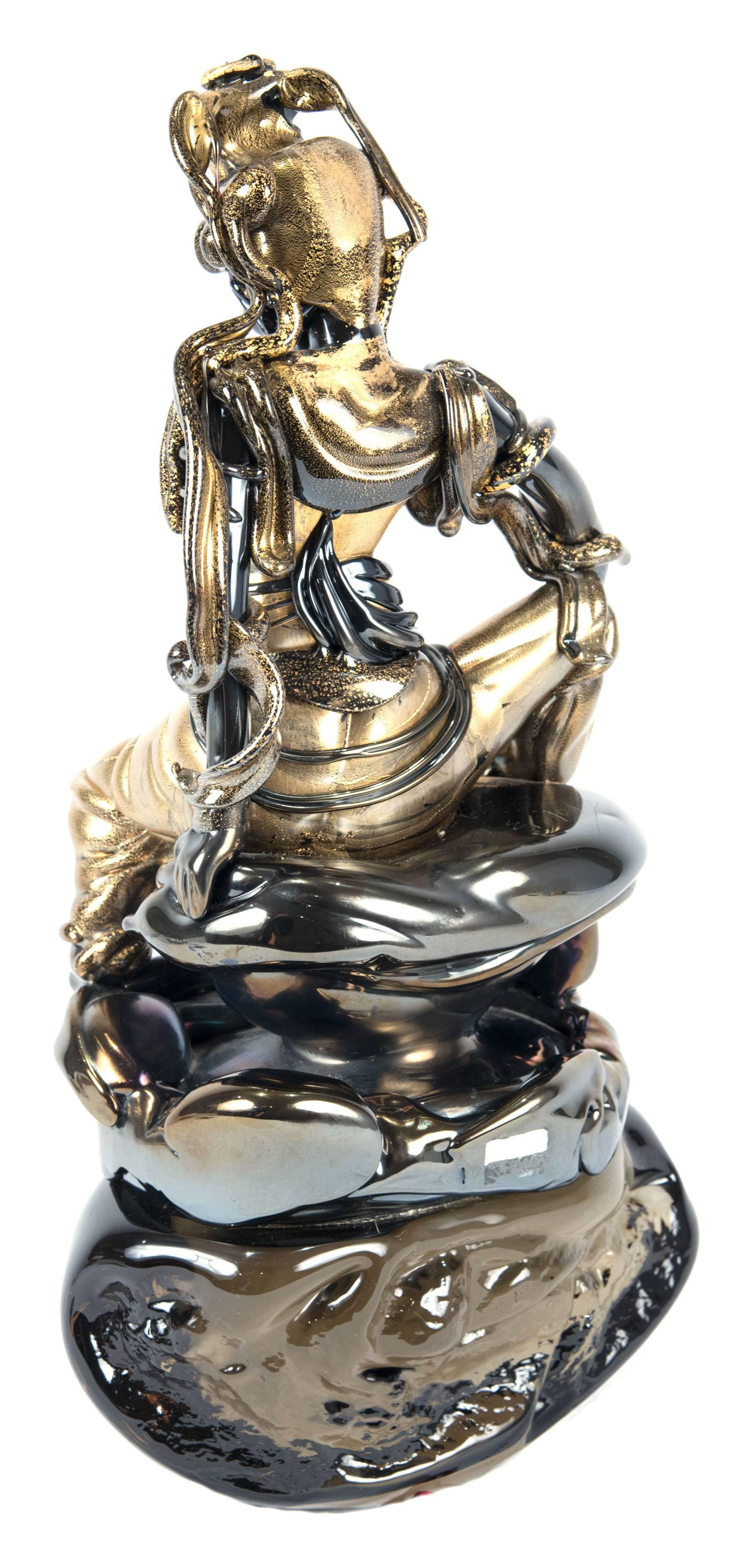 An iridescent glass sculpture made in Murano, Italy depicting the figure of Pavarti, the consort of Shiva, sitting on a naturalistic base, dressed in flowing robes and an elaborate headpiece with long tendrils.