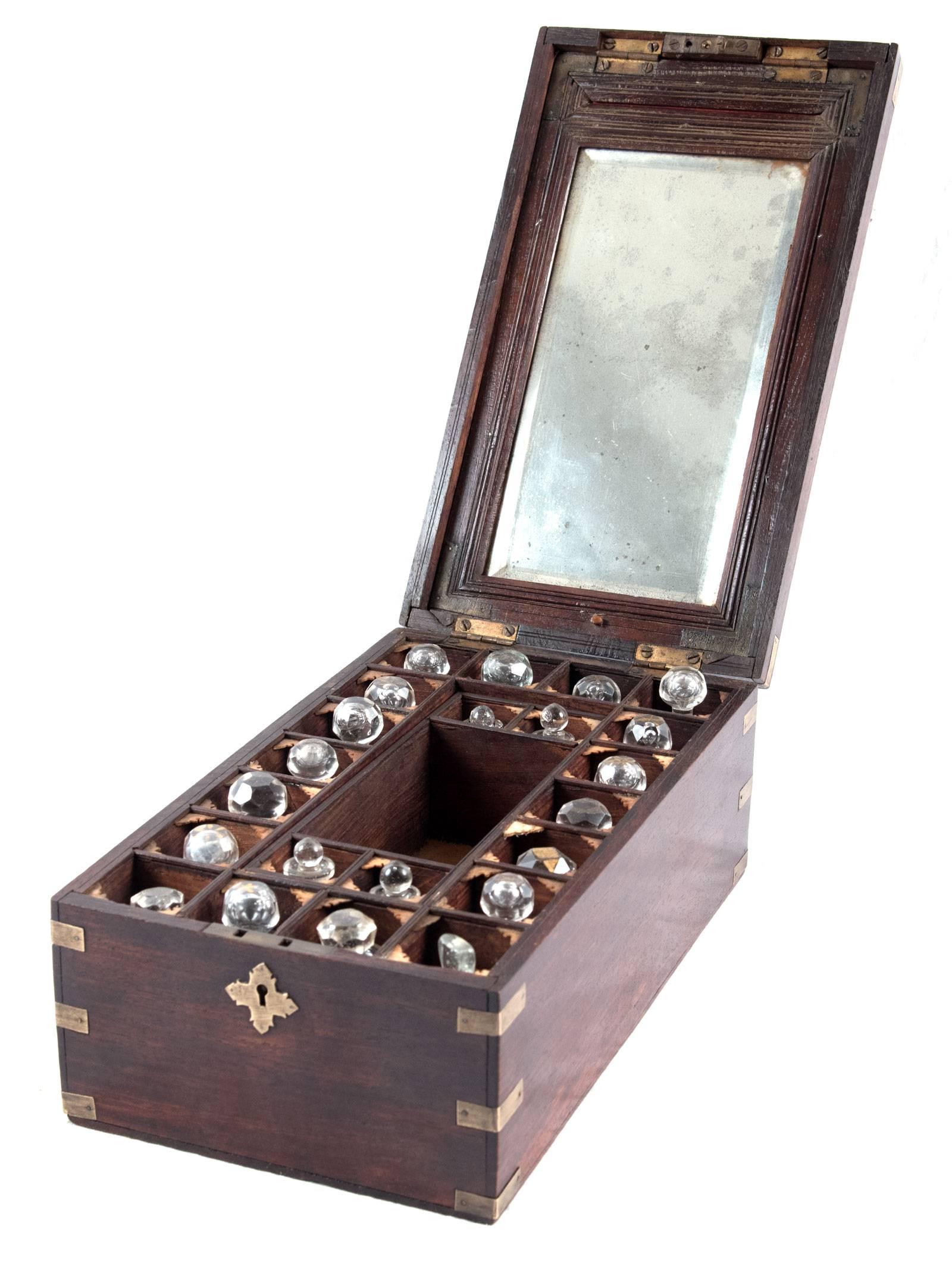 A mahogany apothecary box with a brass-trimmed lid that boarders an inlaid star motif. The box is fitted with a brass escutcheon, the corners edges of the box are fitted with brass mounts. The hinged lid lifts to reveal individual compartments for