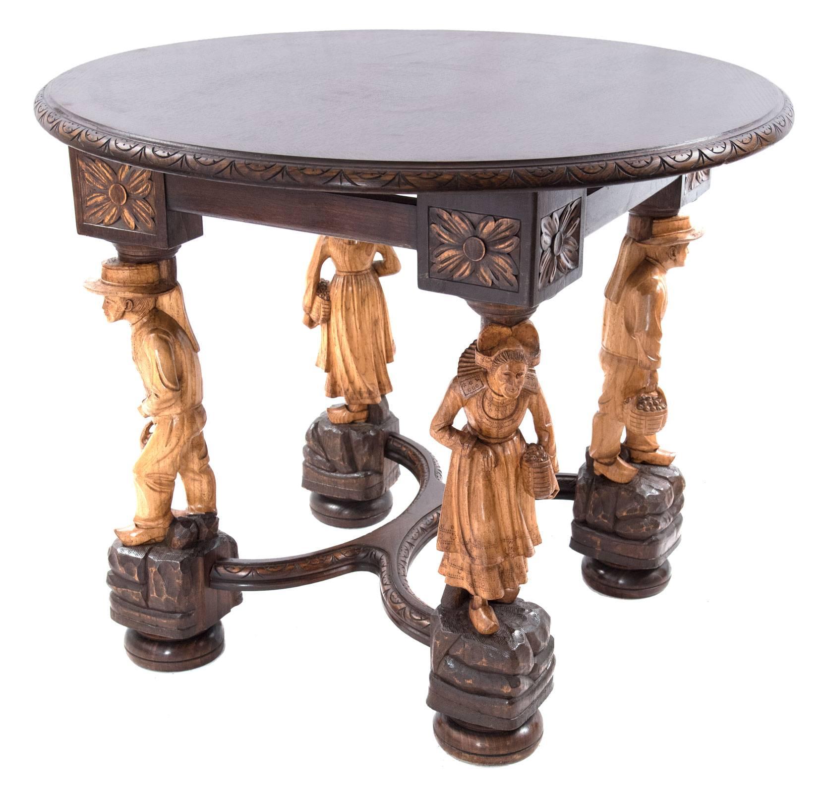 A 19th century carved tiger oak table, its circular top with a carved border above an apron joining square corner blocks that are carved with floral motif, each supported by figural legs of contrasting light wood that are raised on rockwork base and