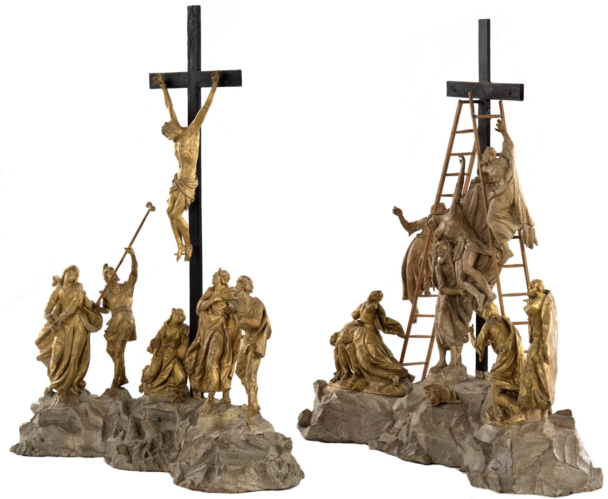 A set of finely hand-carved wooden figural scenes, decorated with gold leaf, depicting two integral events of the crucifixion of Christ. In each composition, figural groupings surround the cross that is mounted into the naturalized rocky ground; the