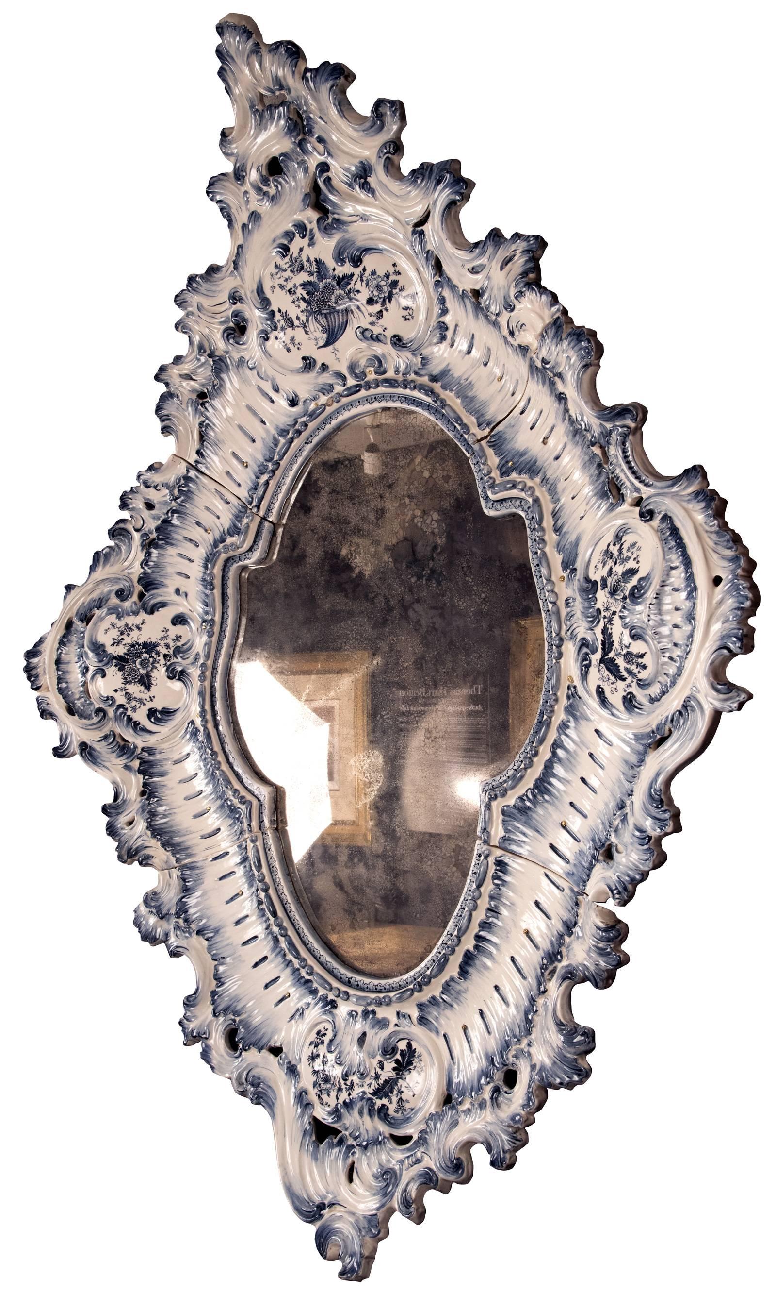 A blue and white Rococo-style porcelain mirror of diamond form with slightly turned in corners, a scrolling filigree border encompassing four cartouches with floral motifs and a centre shaped opening that is back mounted with a metal mirror plate.