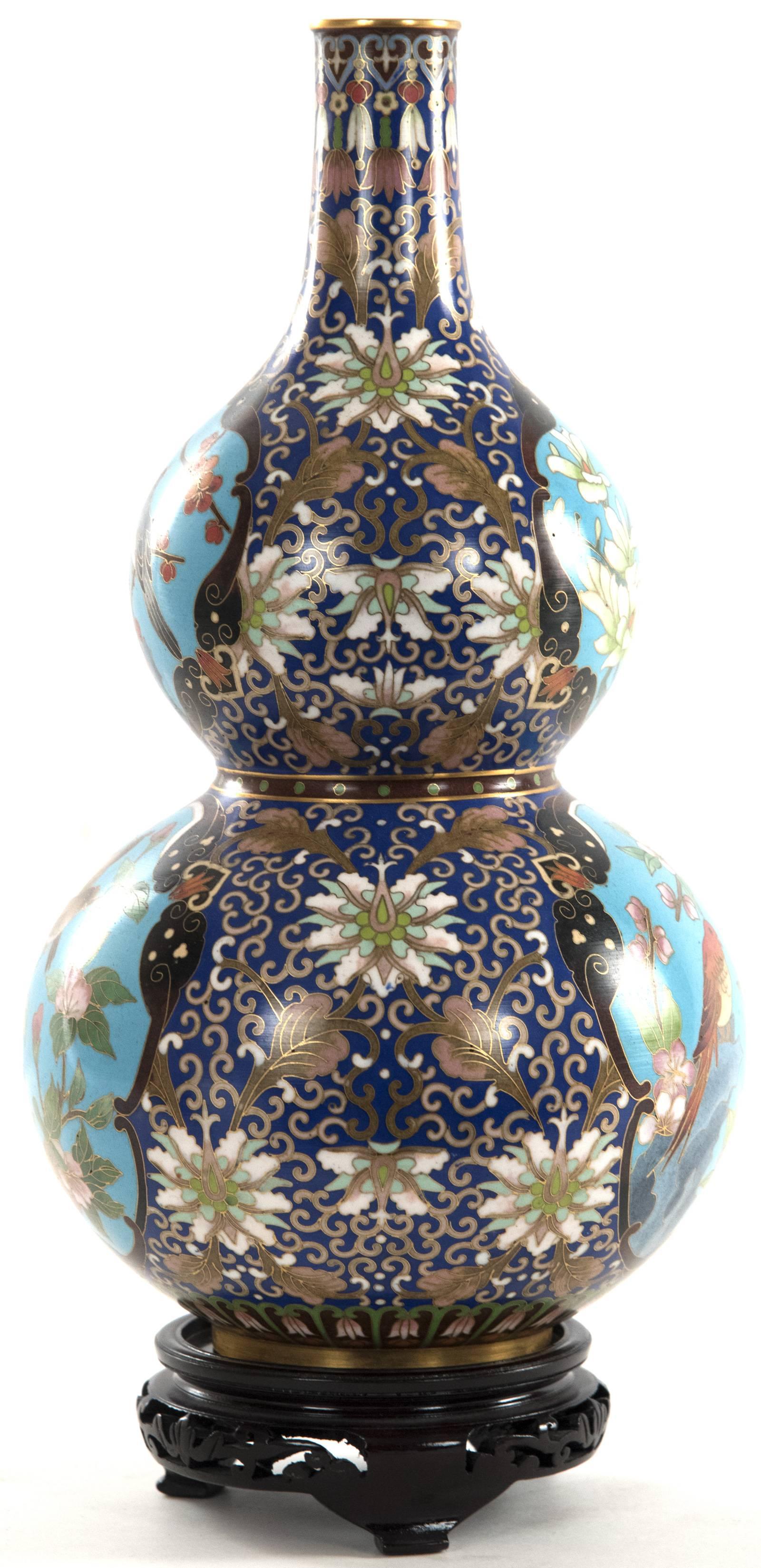 A 20th century Chinese cloisonné enamel vase of double gourd form supported on a carved and pierced wood stand. The vase is fully decorated with the dark blue ground richly covered with scrolling filigree and florals and cerulean cartouches