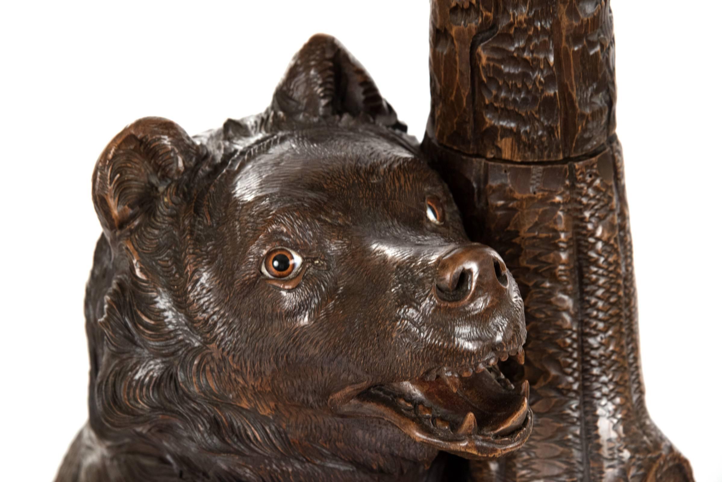 A 19th century carved linden wood black forest bear hall tree with the large standing bear, mouth open and glass eyes watching cubs above, on a naturalistic base that incorporates a crescent shaped drip tray, its one paw supporting a looped branch