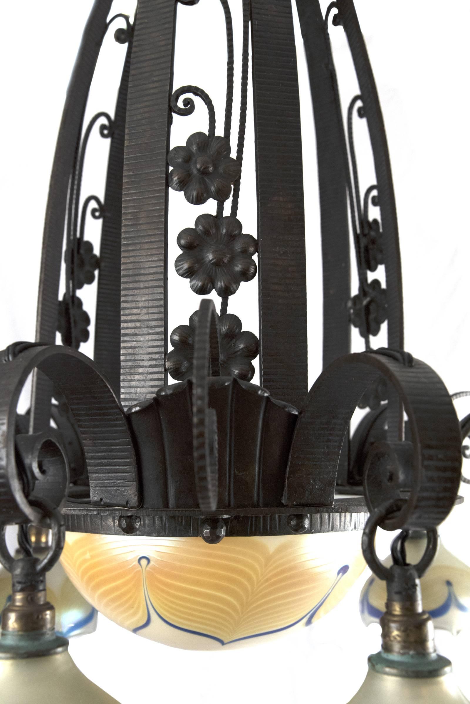 A 20th century, circa 1925, wrought iron chandelier in the Art Deco style of Edgar Brandt with the hanging support set within a blossoming tulip-shaped cap, above three domed supports decorated with applied flowers, beneath which the central pulled