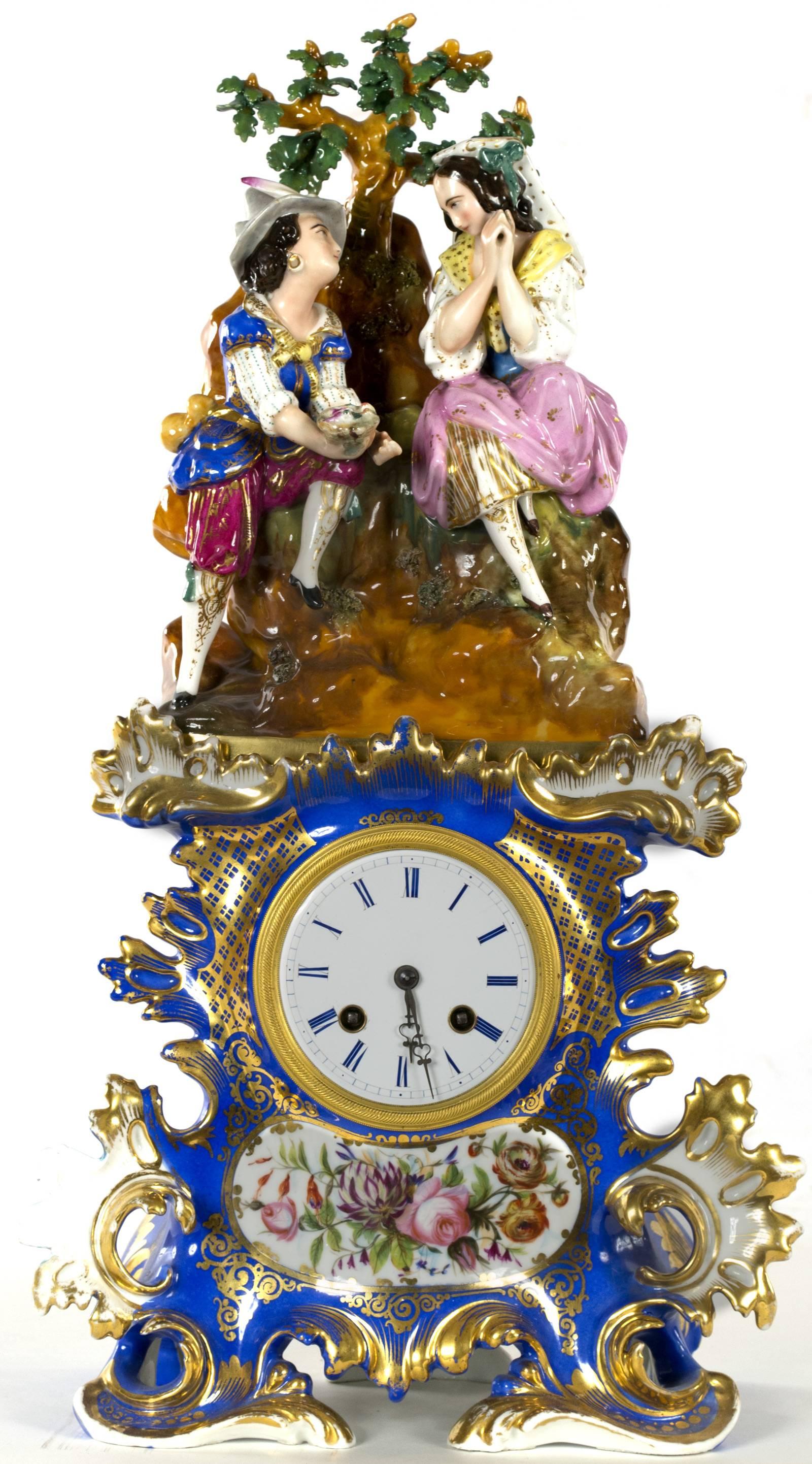 A two piece Old Paris porcelain clock. The top half features a figurative group of a romantic couple, courting one another beneath the branches of a tree. The bottom half houses the clock gilt and painted with bright colors. Made in France during